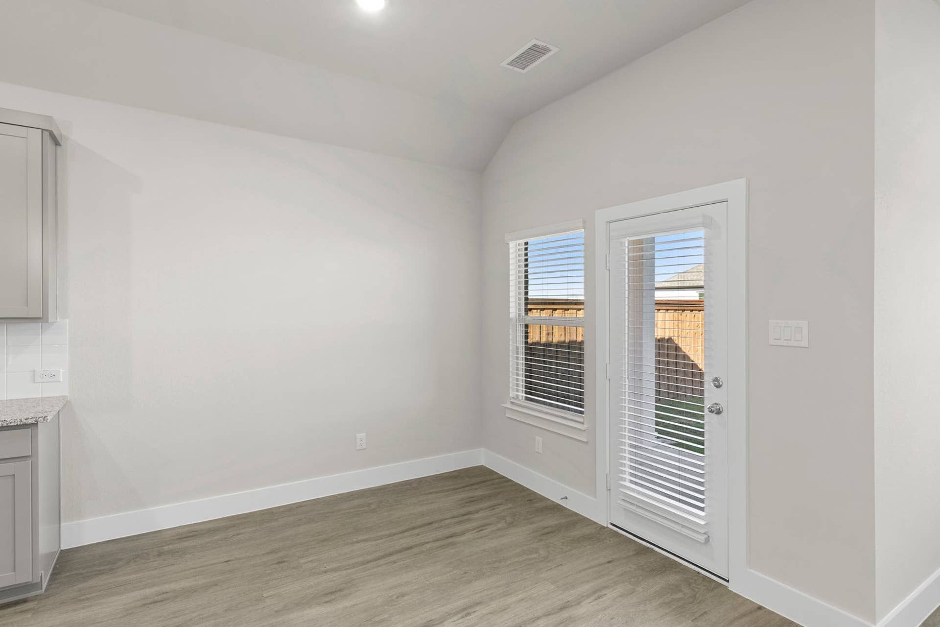 Bright dining area with wood flooring and patio door with blinds.