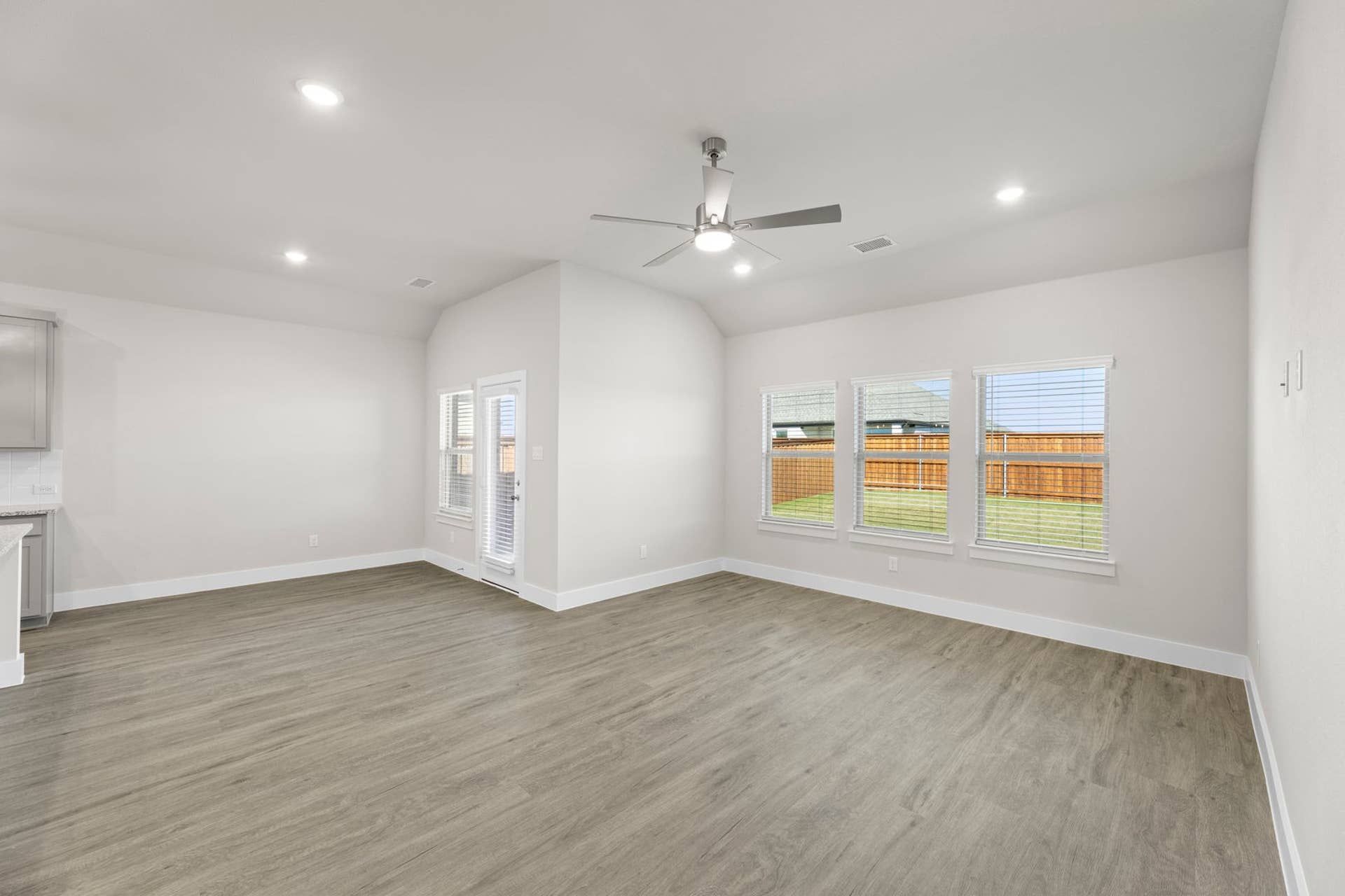 Spacious living room with wood flooring, ceiling fan, and large windows.