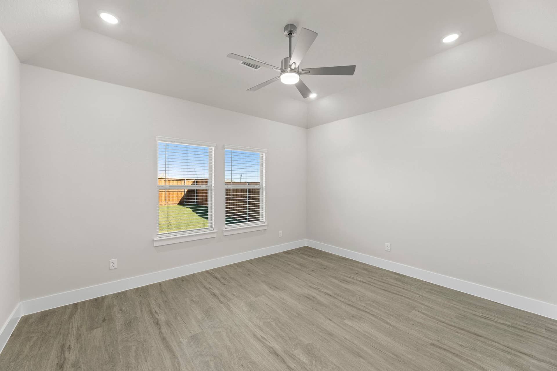 Spacious, bright room with ceiling fan and large windows overlooking backyard.