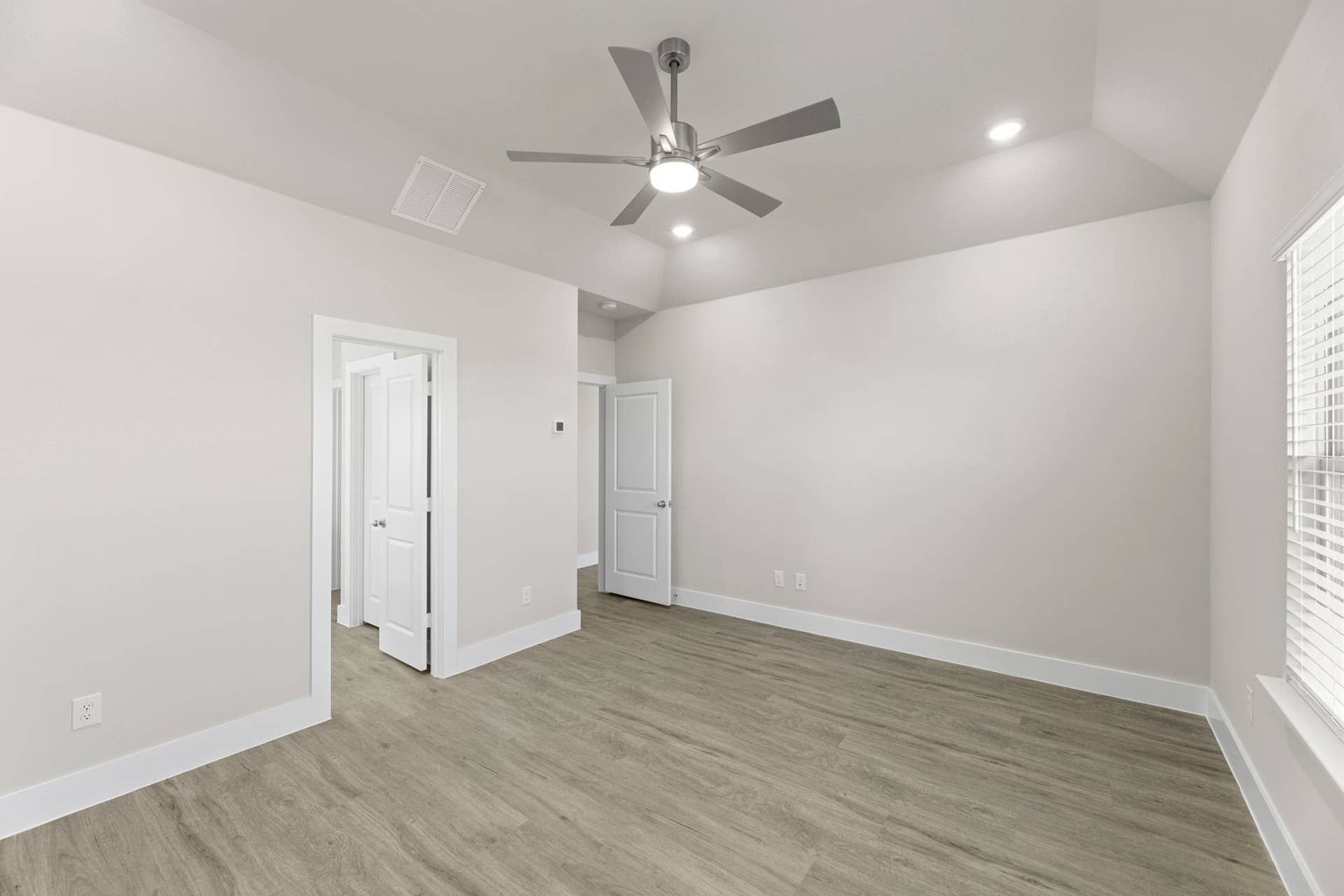 Spacious room with wood flooring, ceiling fan, and ample natural light.