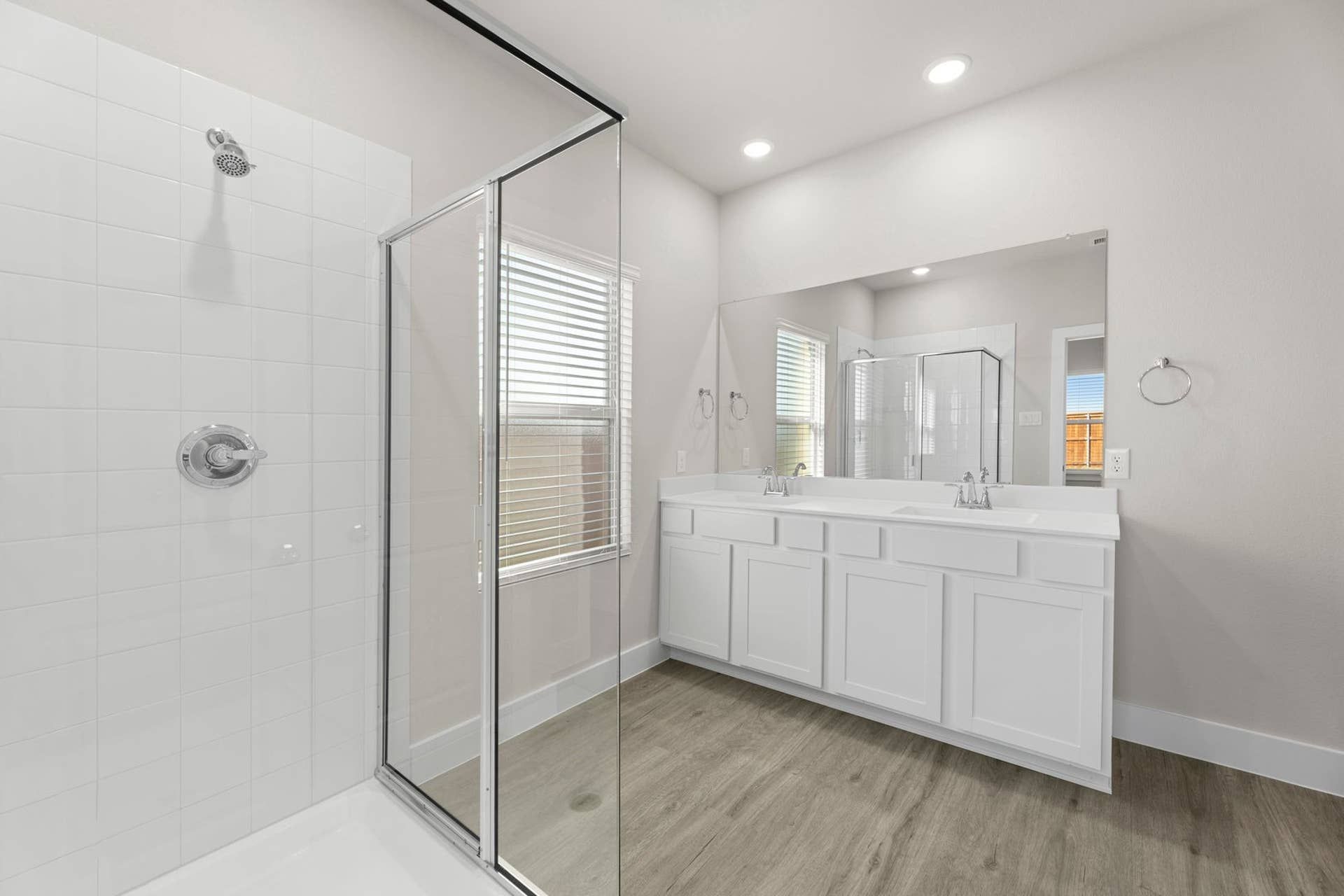 Modern bathroom with glass shower, dual sinks, and natural light.