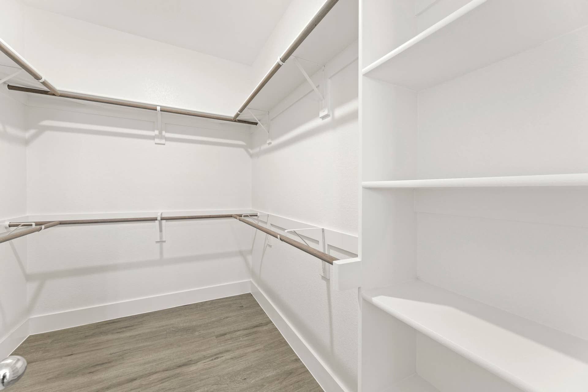 Spacious walk-in closet with wooden rods and white shelving.