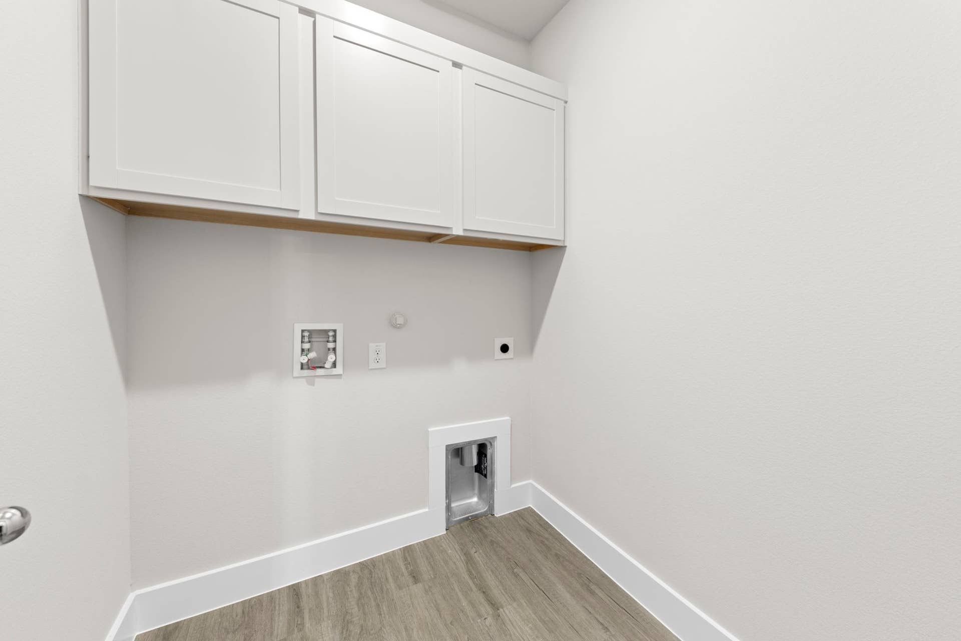Utility room with white cabinets and laundry hookups.