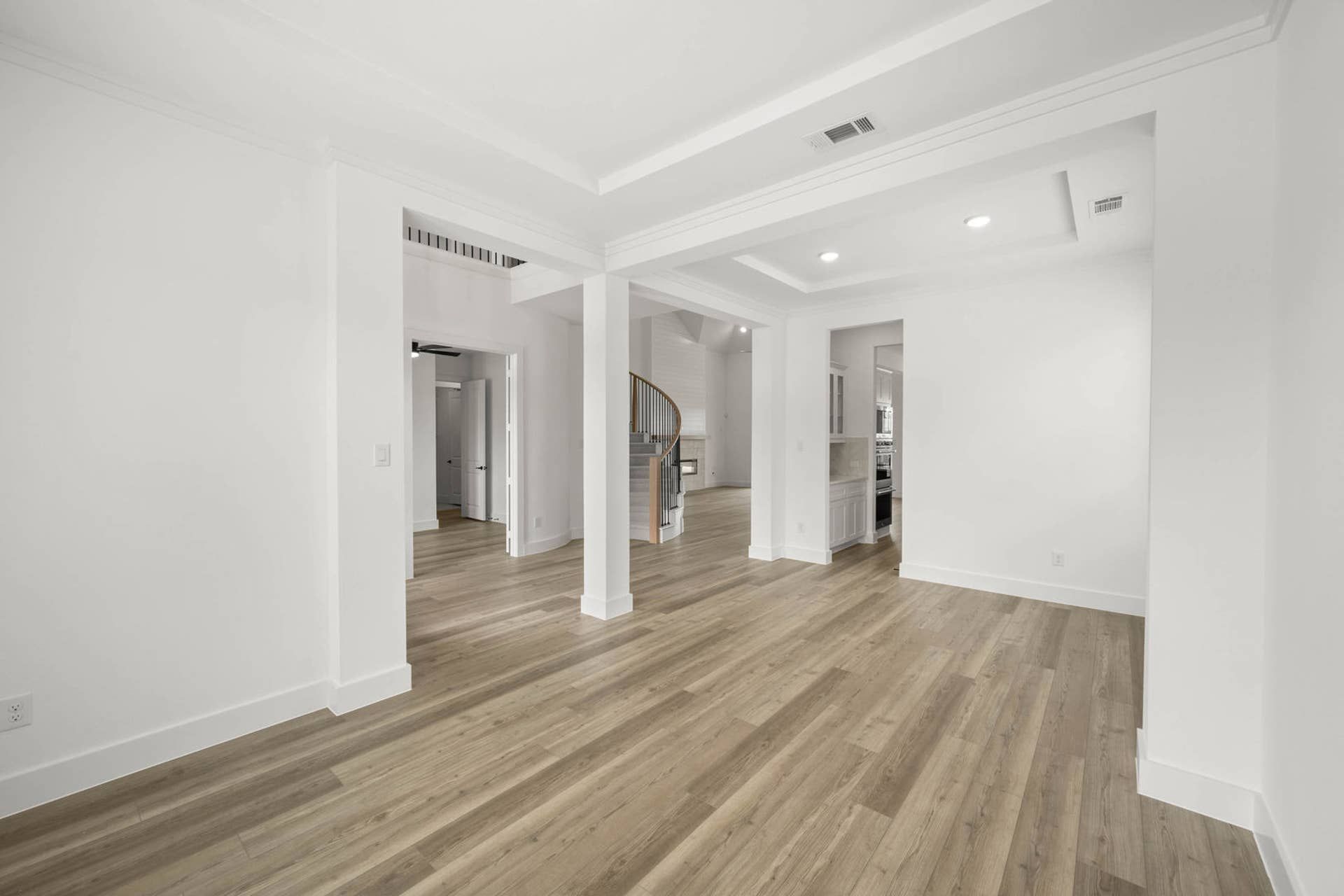 Spacious interior flex room with tray ceilings, wood-look floors, and open view to staircase