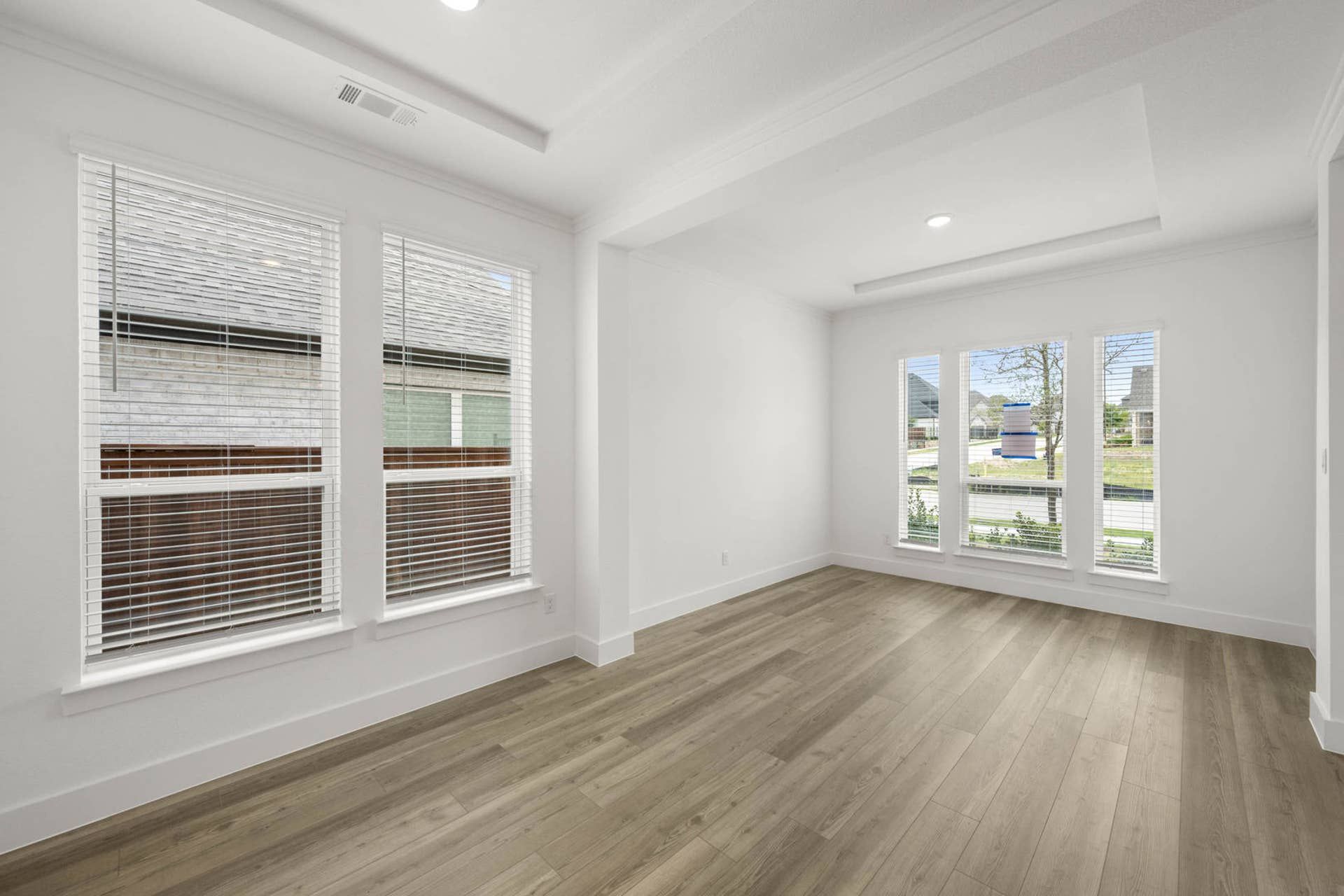 Bright interior flex space with tray ceiling, wood-look floors, and large front-facing windows