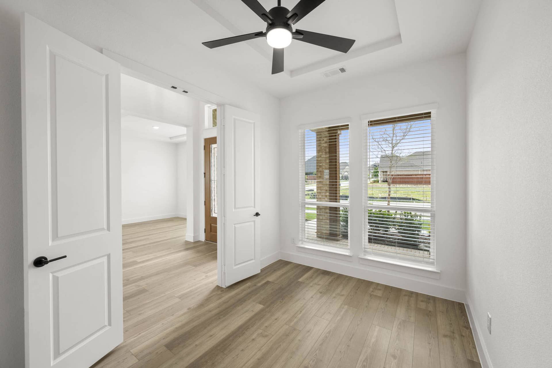 Bright study interior with wood-look flooring, tray ceiling, ceiling fan, and front-facing windows
