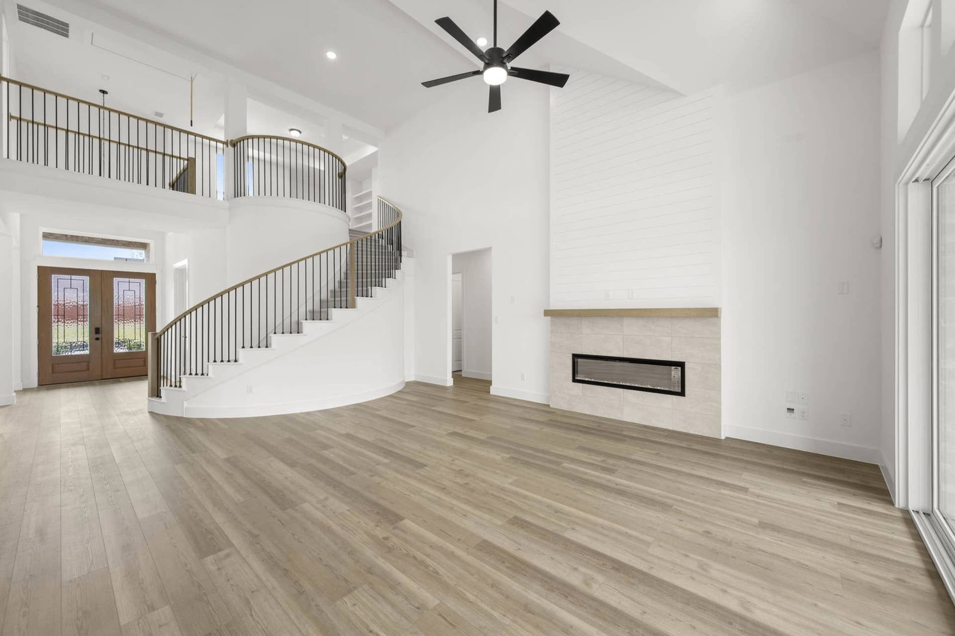 Open living room with curved staircase, soaring ceilings, fireplace, and wood-look flooring