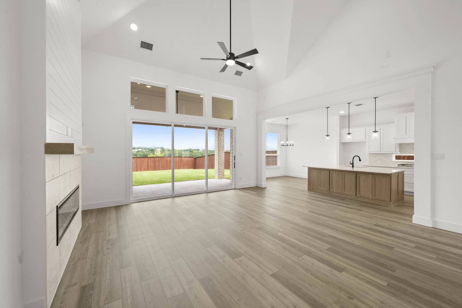 Open-concept living room with vaulted ceiling, fireplace, sliding glass doors, and adjacent kitchen island