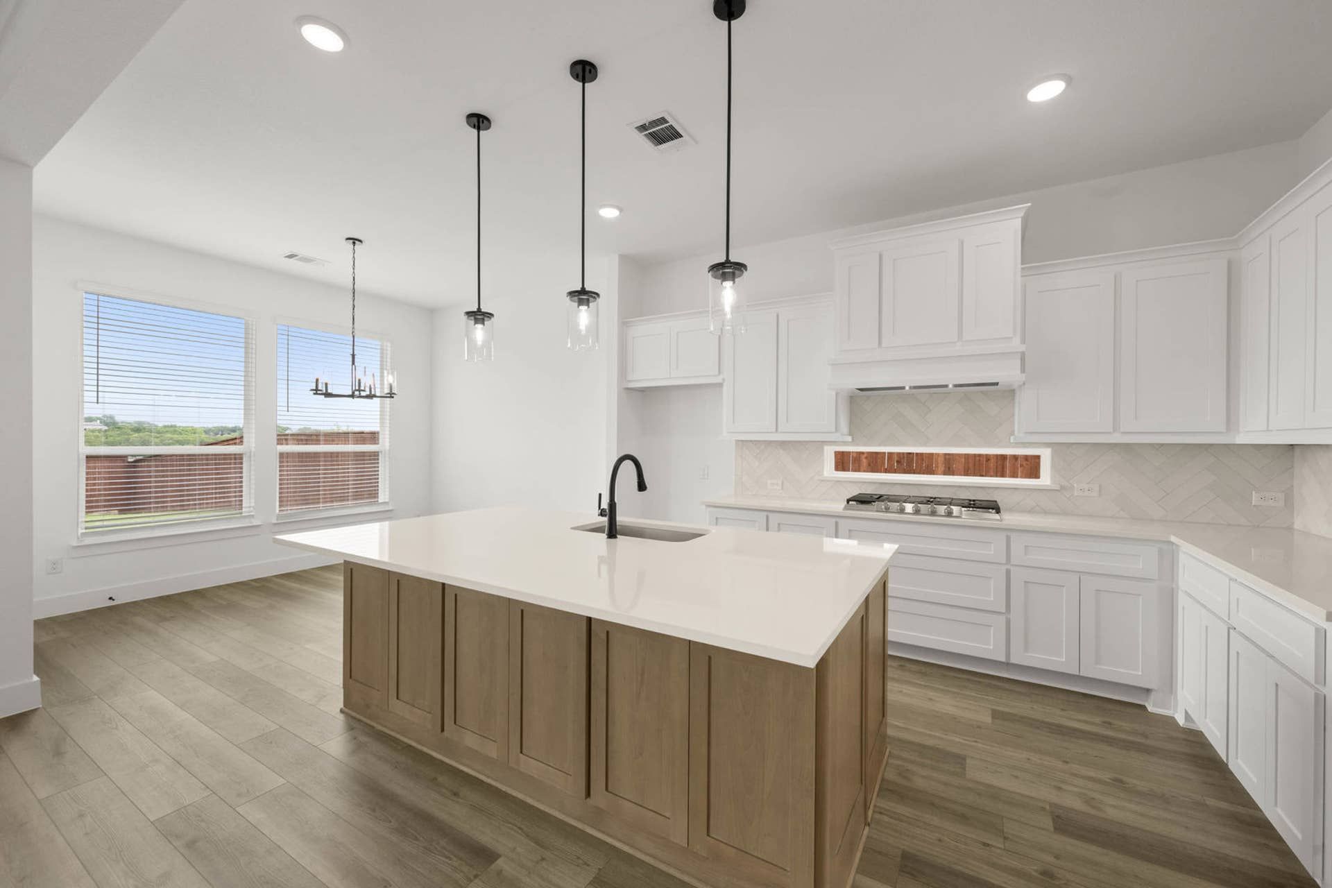 Bright interior kitchen with large island, white cabinetry, pendant lighting, and herringbone backsplash