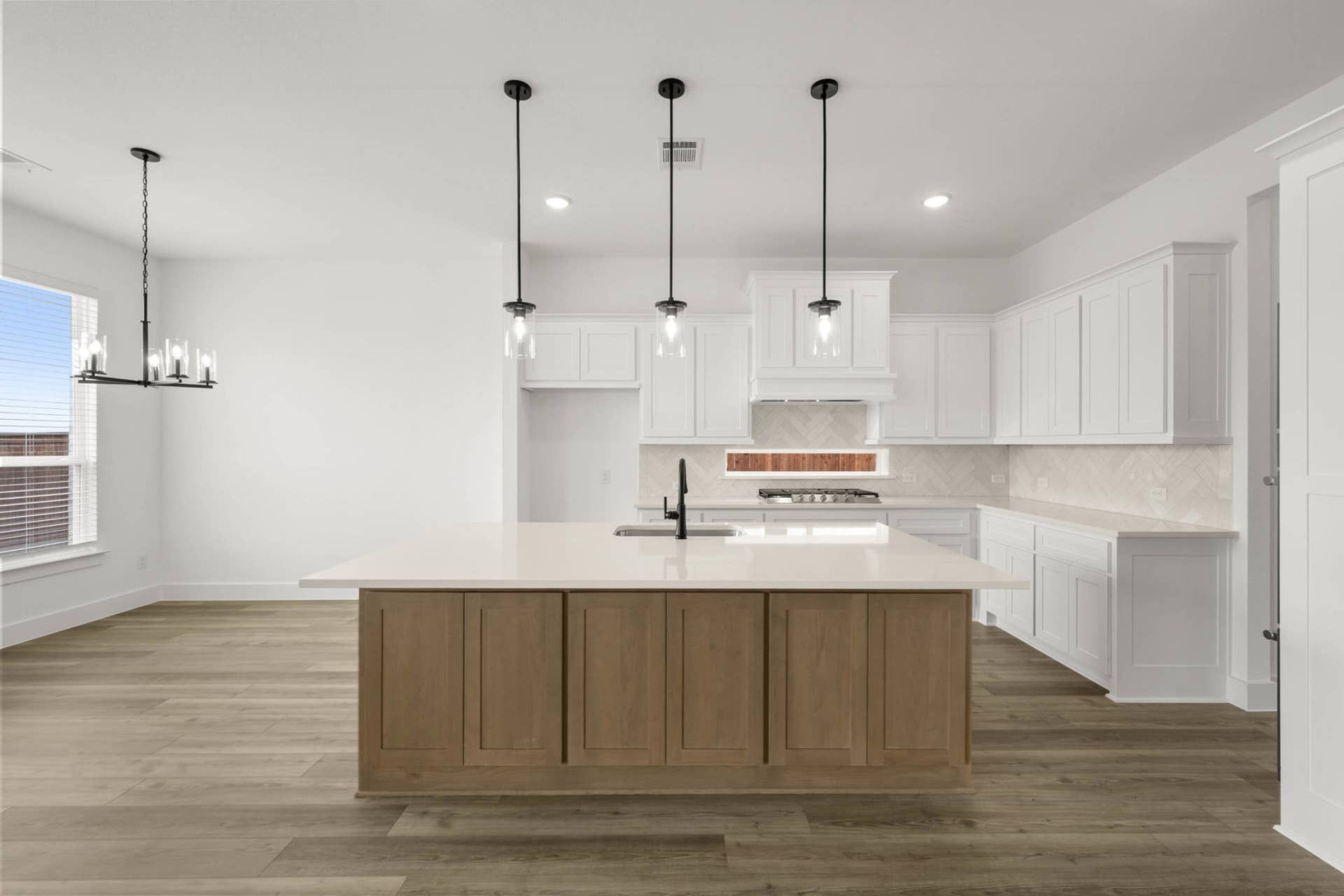 Bright kitchen interior with large island, white cabinetry, pendant lighting, and herringbone backsplash