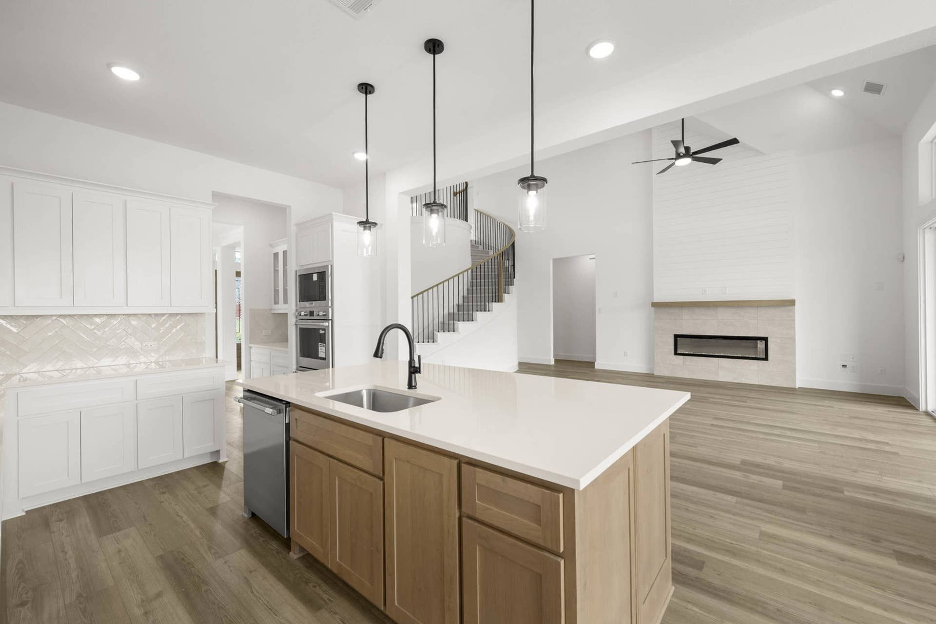 Open-concept interior with kitchen island, pendant lighting, curved staircase, and modern fireplace