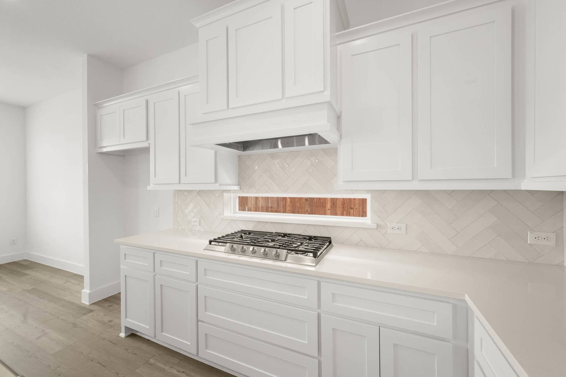 Kitchen interior with white shaker cabinets, gas cooktop, vent hood, and herringbone tile backsplash