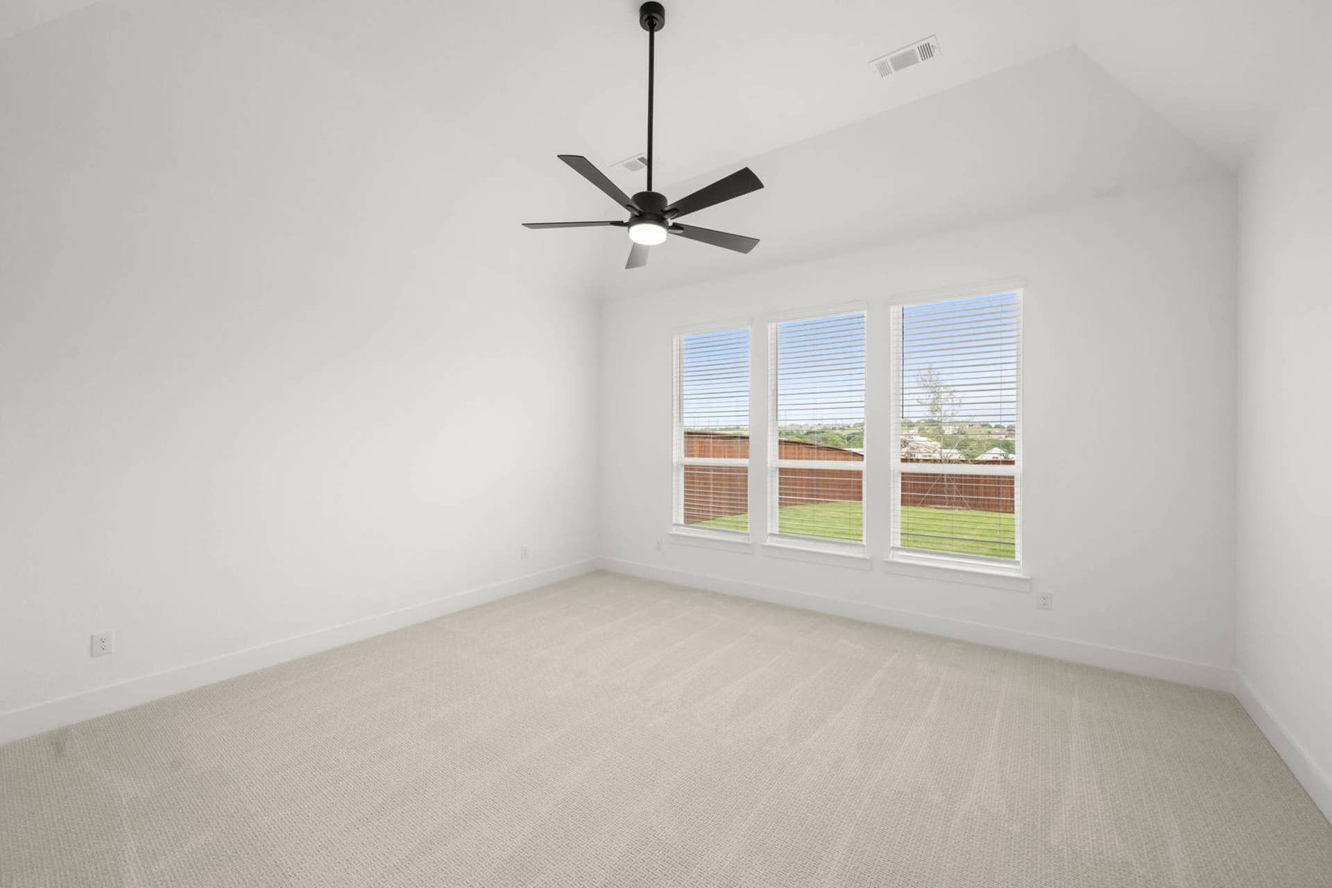 Primary suite interior with vaulted ceiling, ceiling fan, carpet flooring, and three bright windows