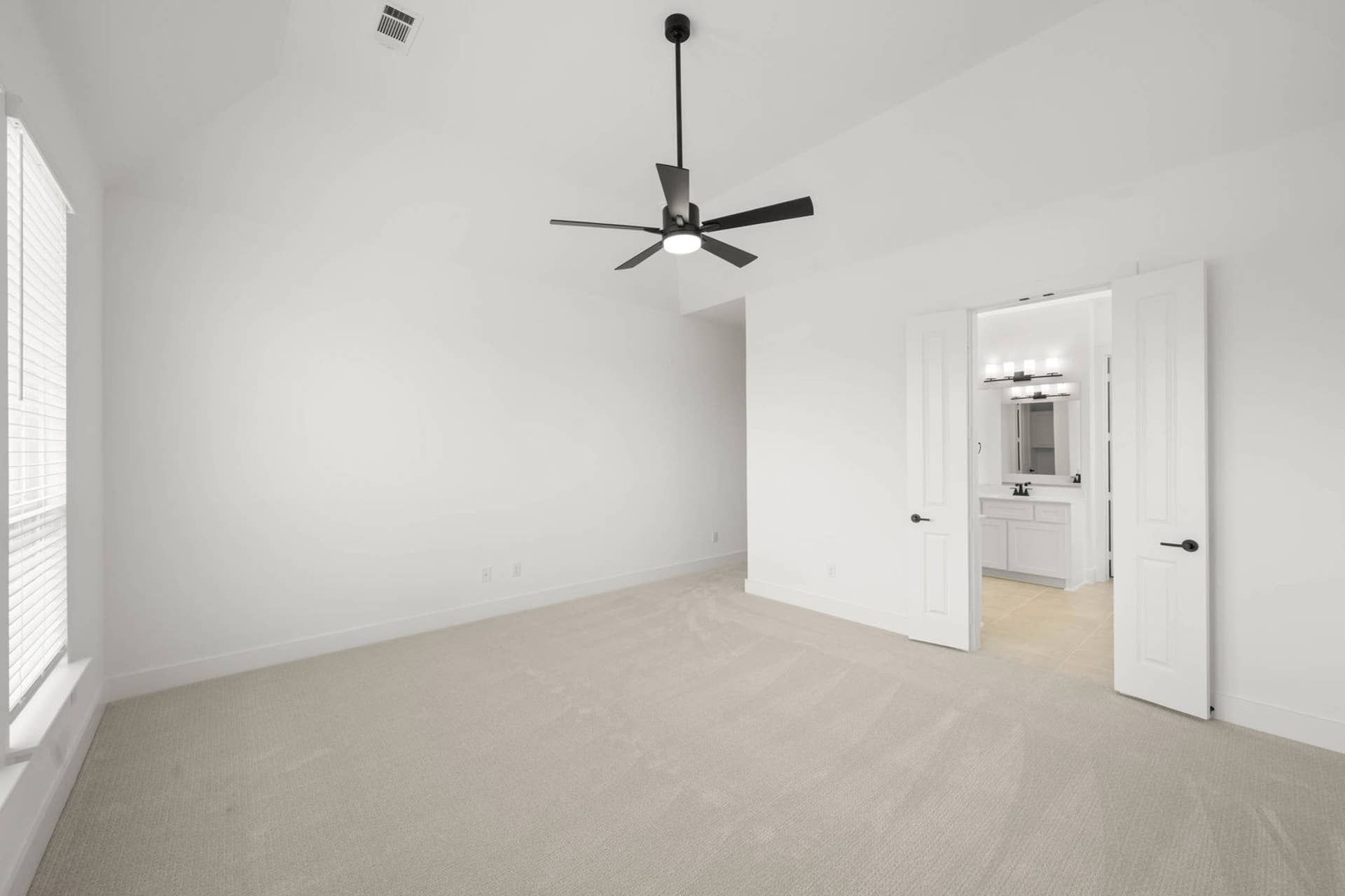 Primary suite interior with vaulted ceiling, ceiling fan, and ensuite bath entry