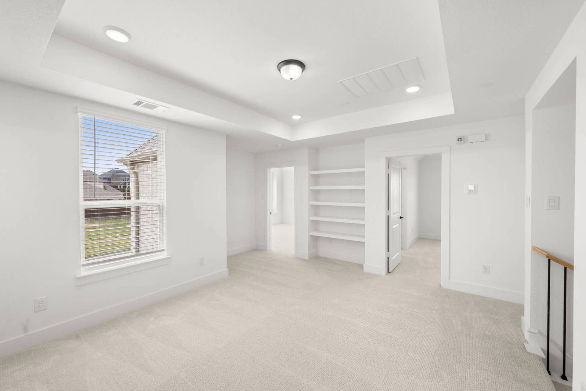 Bright loft interior with tray ceiling, built-in shelves, carpet, and large window
