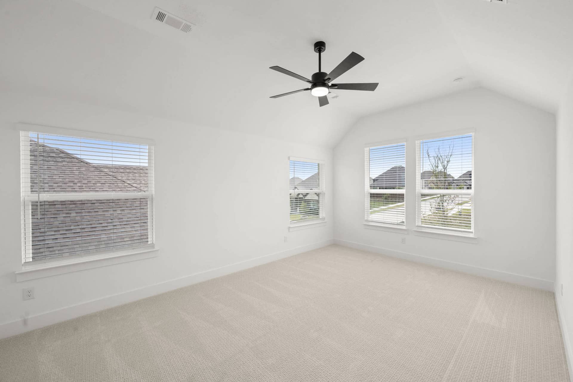 Bright secondary suite bedroom with vaulted ceiling, carpet flooring, ceiling fan, and multiple windows