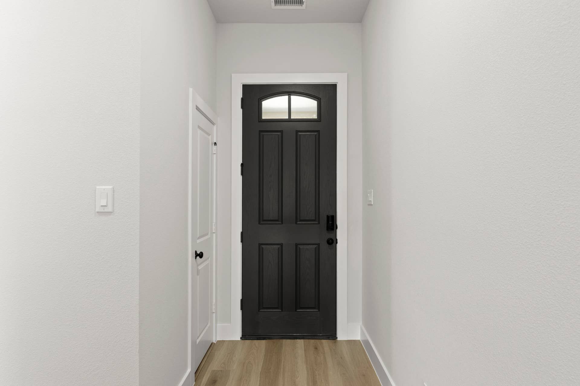 Interior entry hallway with black front door, transom window, and light wood flooring