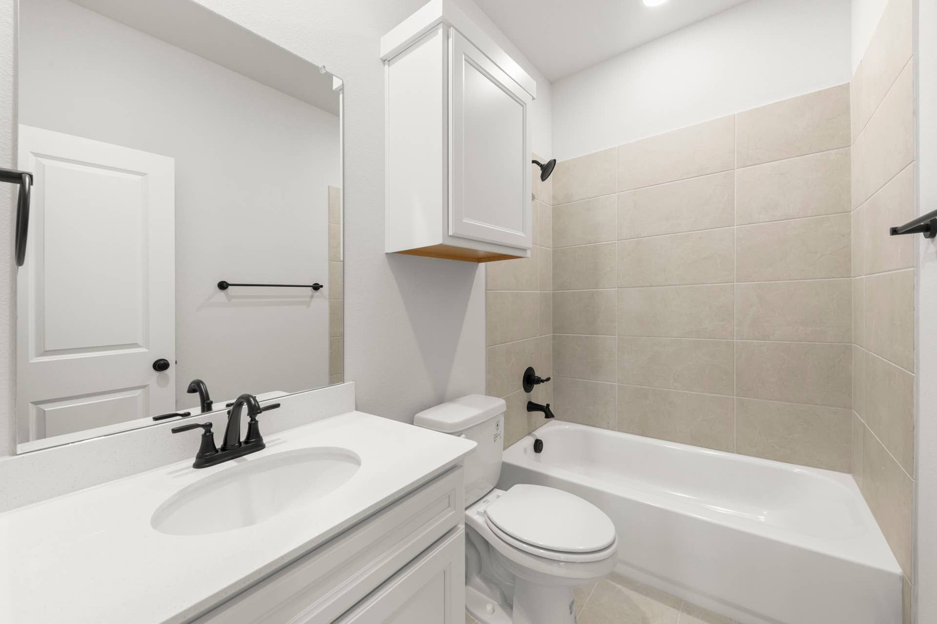 Secondary bathroom with white vanity, tub-shower combo, tiled surround, and black fixtures