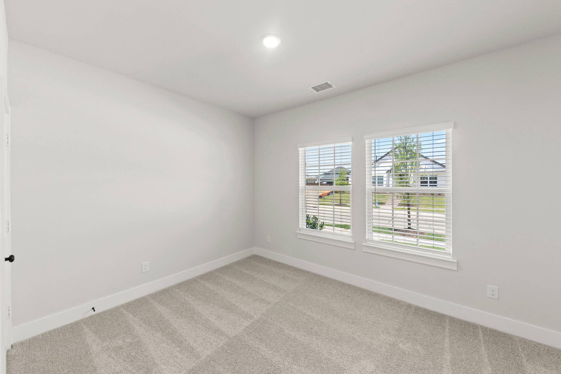 Bright secondary bedroom with plush carpet, neutral walls, and two front-facing windows.