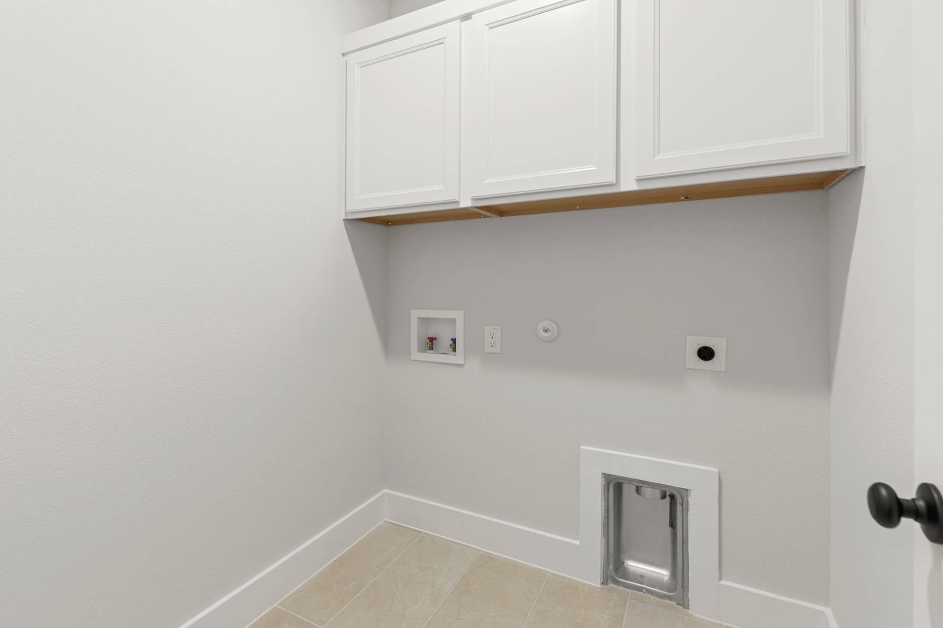 Utility room interior with upper cabinets, washer-dryer hookups, and tile flooring