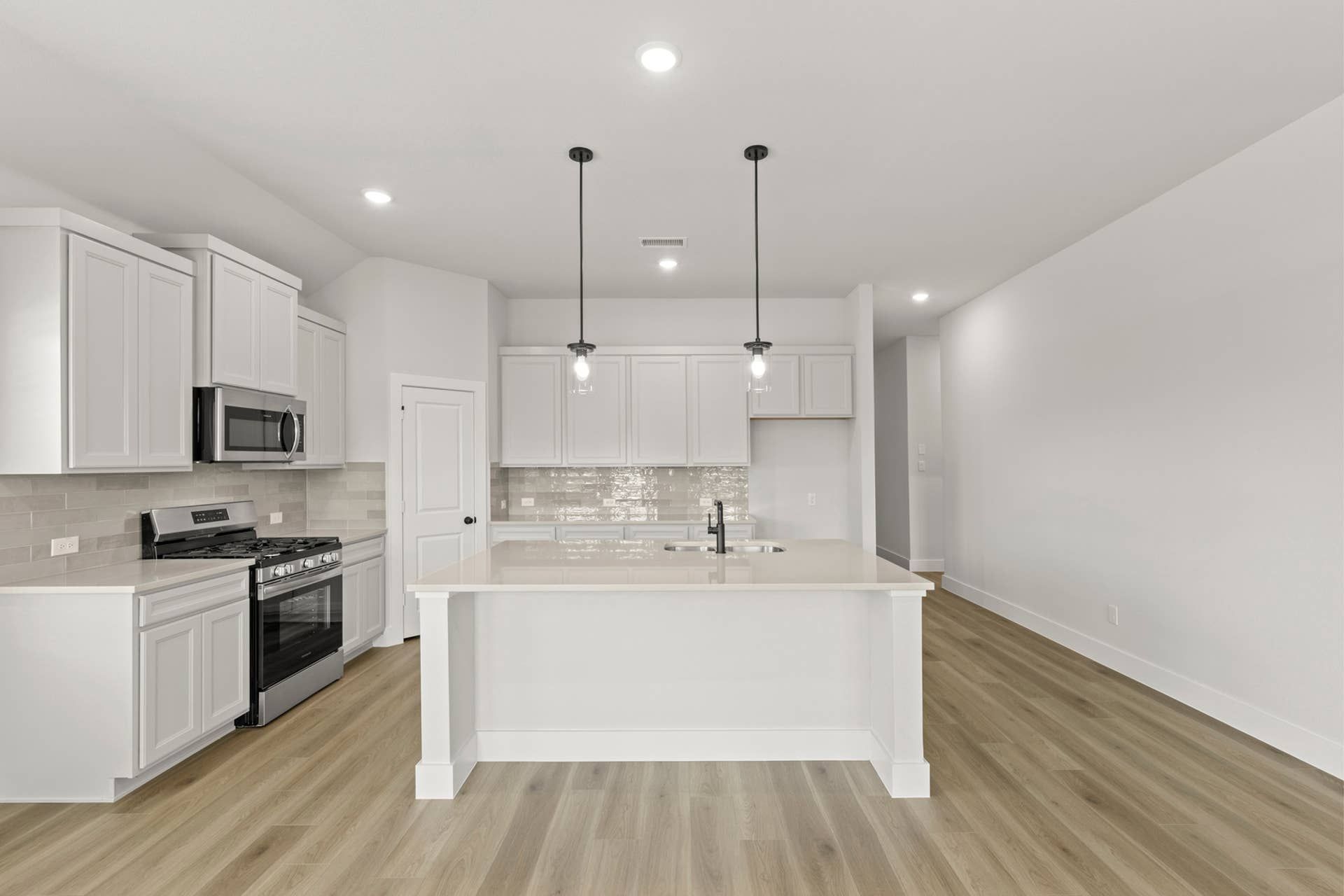 Interior kitchen with white cabinets, island sink, pendant lighting, stainless appliances, and wood-look floors