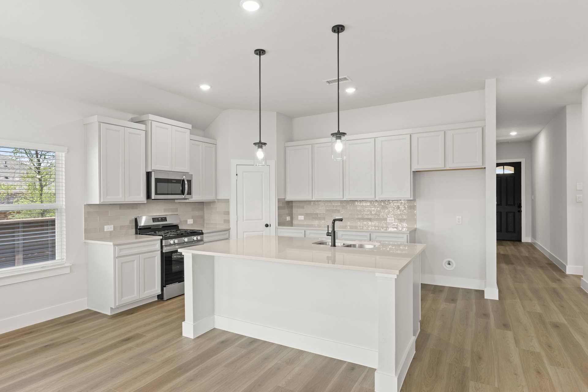Bright kitchen interior with white cabinets, large island, pendant lighting, and stainless steel appliances