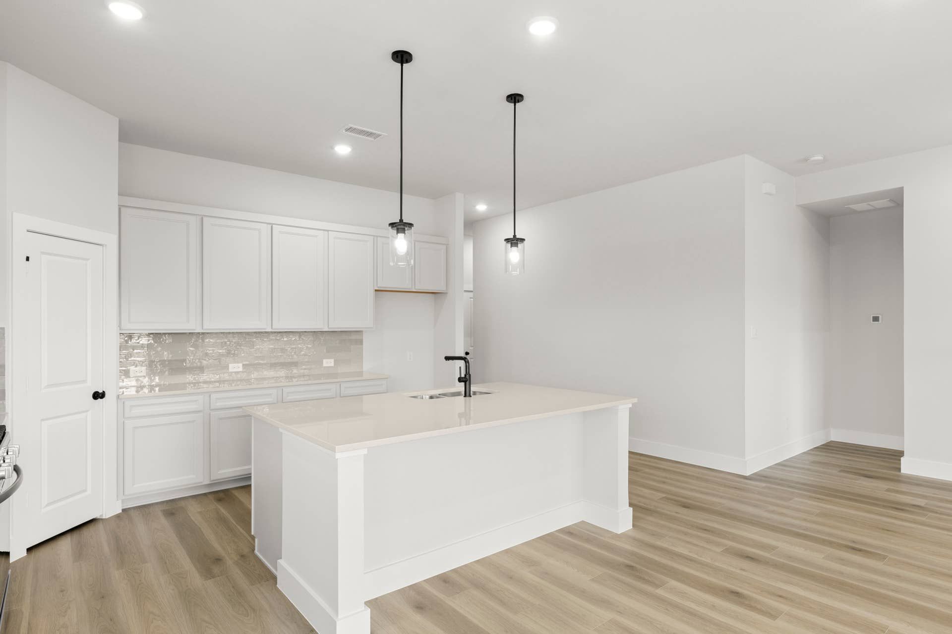 Bright modern kitchen with white cabinets, large island, pendant lighting, and wood-look flooring