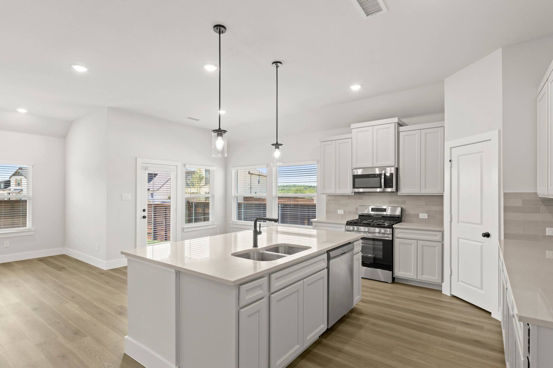 Bright kitchen interior with white cabinetry, large island, stainless appliances, pendant lighting, and pantry.