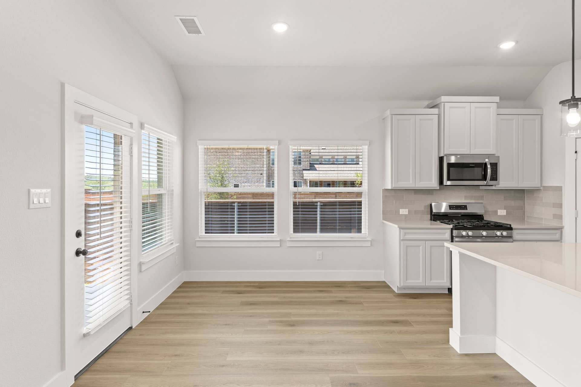 Bright dining area beside kitchen with large windows, patio door, and white cabinetry