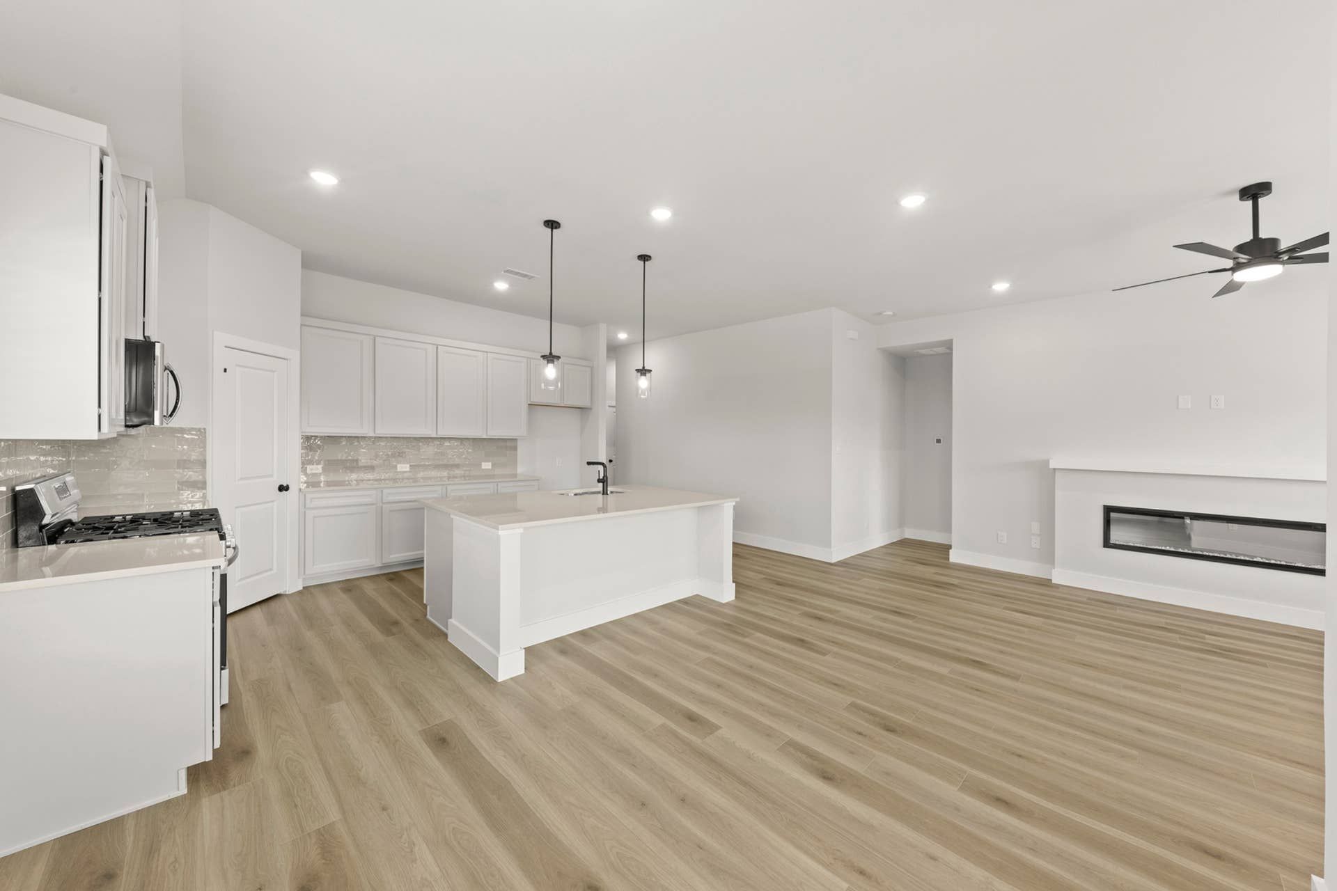 Open-concept interior with white kitchen island, pendant lighting, fireplace, and wood-look flooring