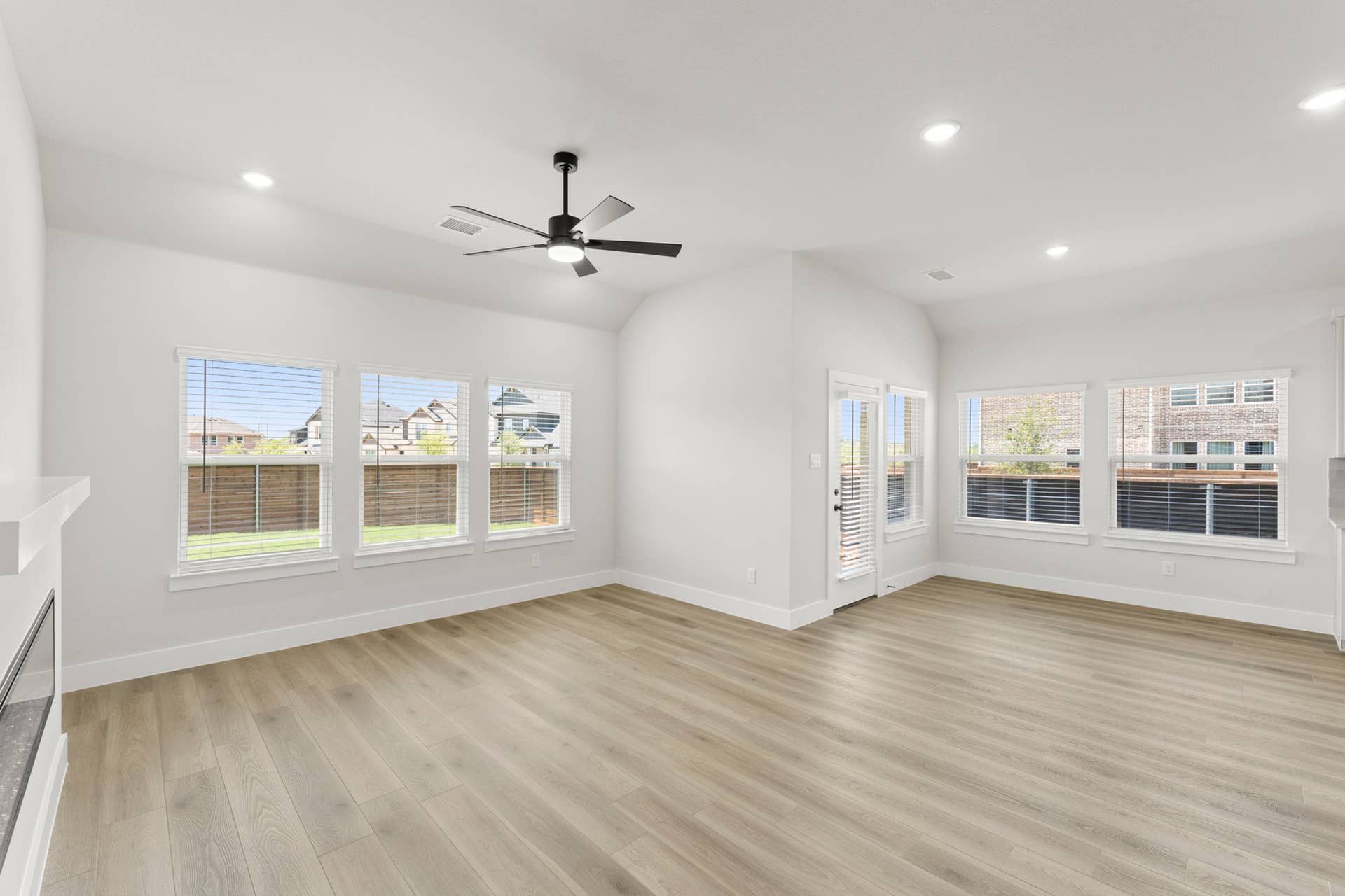 Open family room with vaulted ceiling, wood-look floors, ceiling fan, and abundant windows