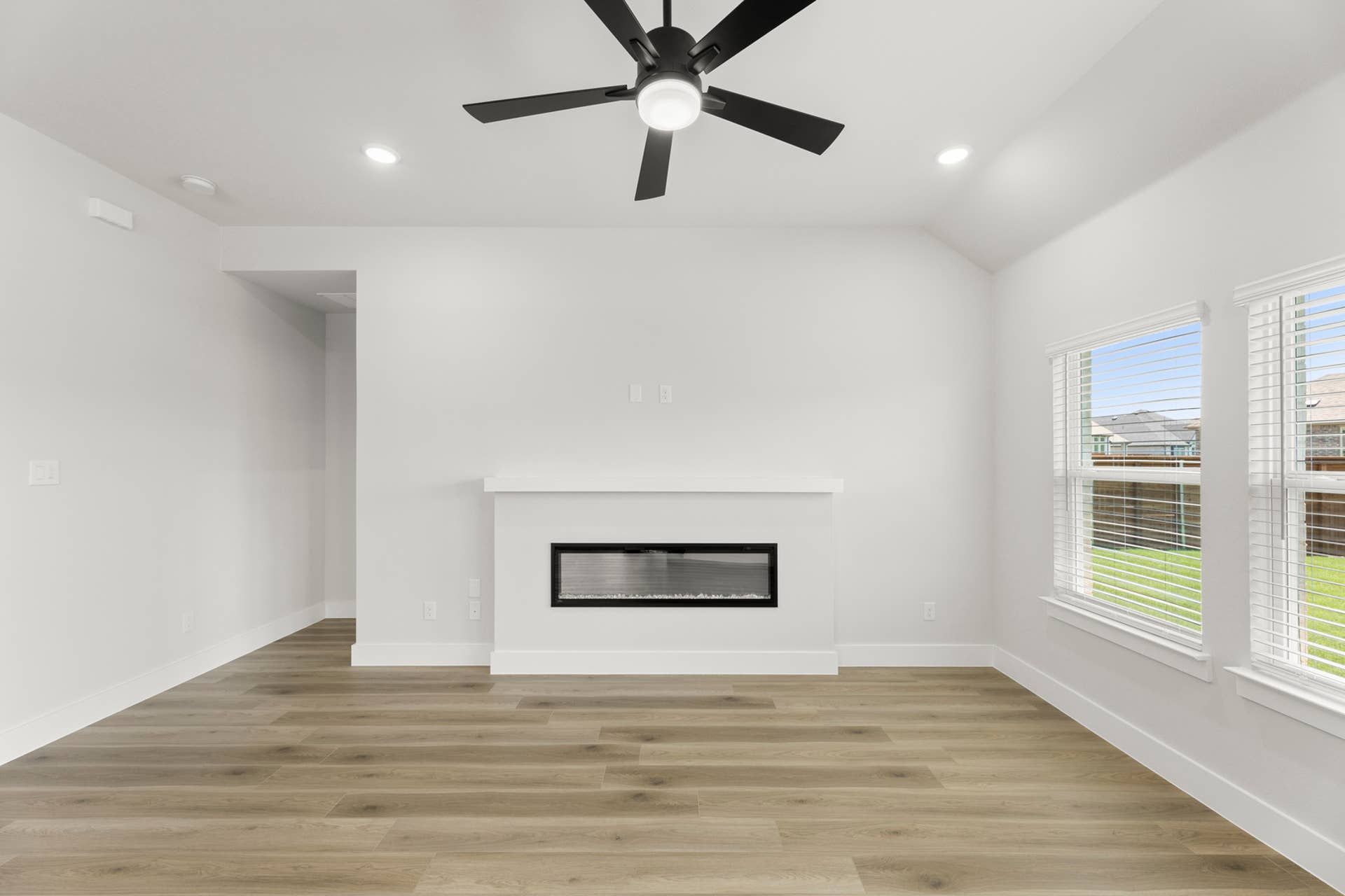 Bright family room with linear fireplace, vaulted ceiling, ceiling fan, and large windows