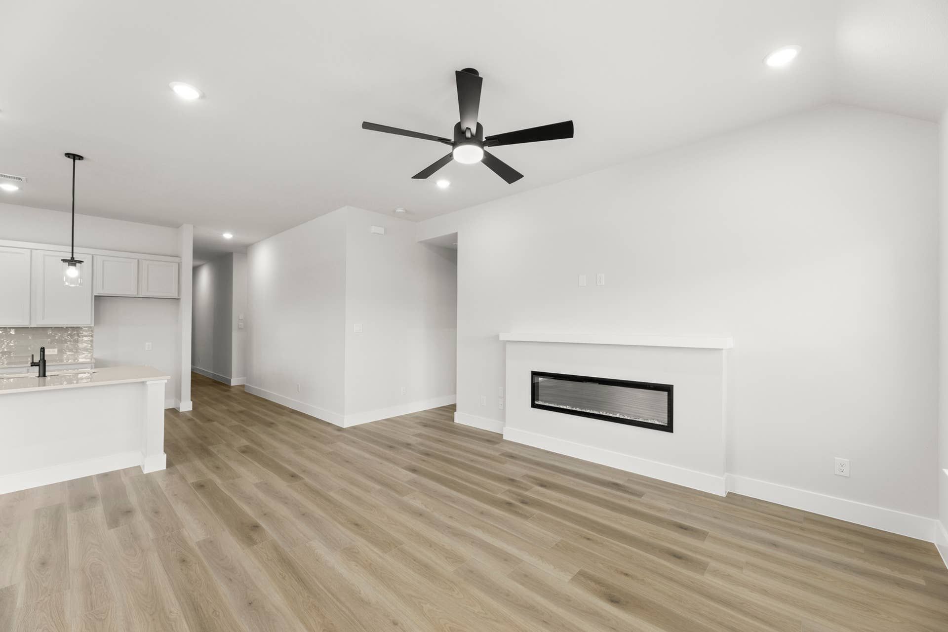 Open-concept living room with linear fireplace, ceiling fan, wood-look floors, and adjacent kitchen