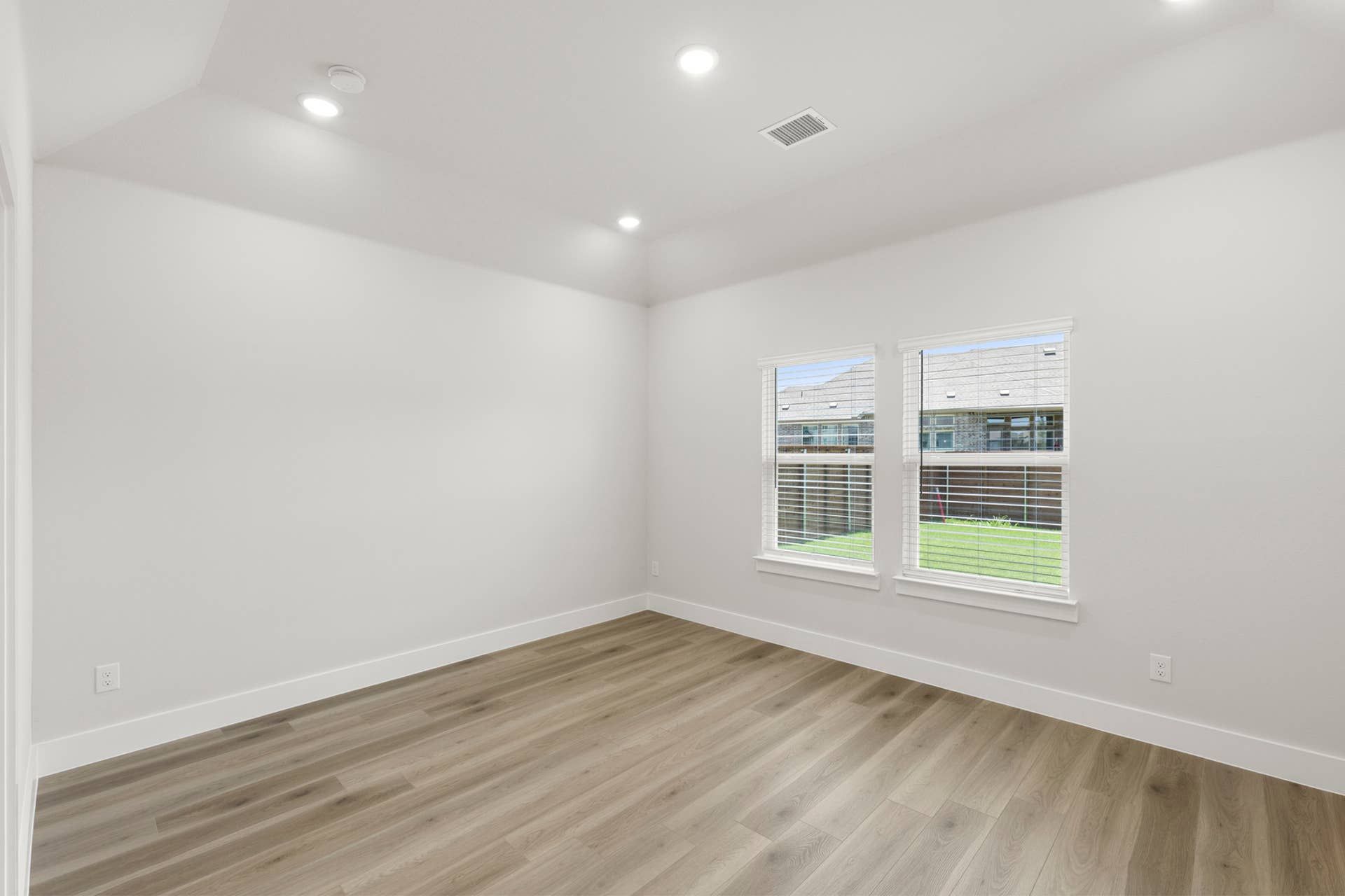 Primary bedroom with wood-look flooring, recessed lighting, and two backyard-facing windows