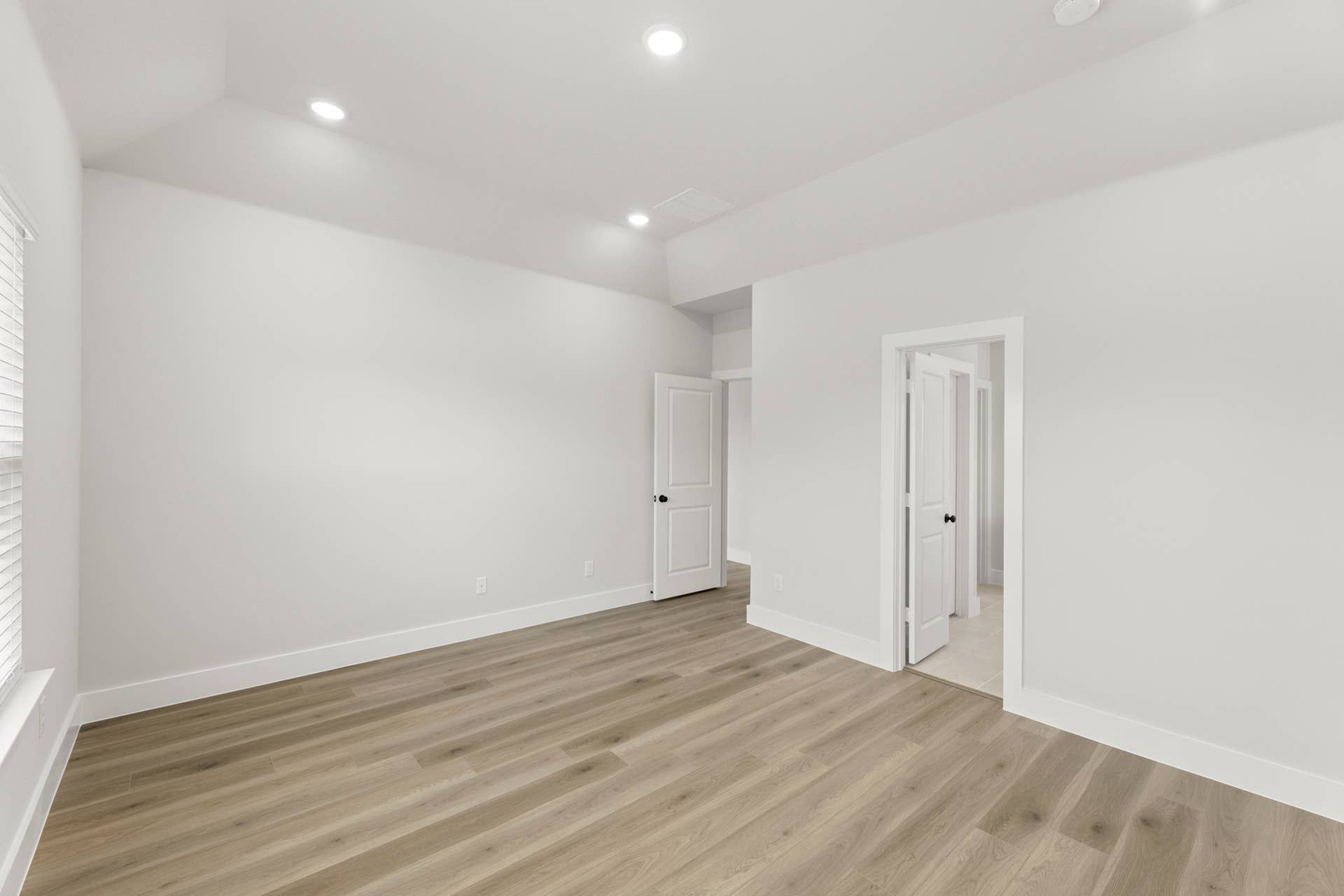Primary bedroom interior with tray ceiling, recessed lighting, wood-look floors, and ensuite access