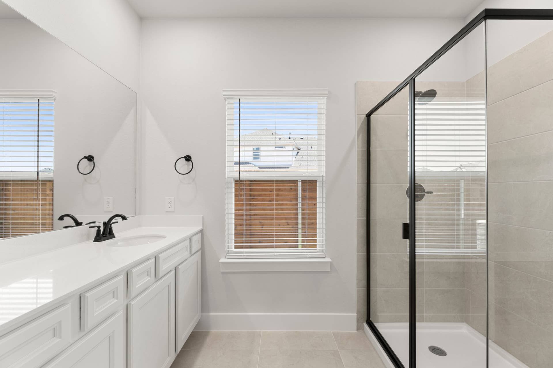 Primary bathroom interior with dual-sink vanity, large mirror, and glass-enclosed tiled shower