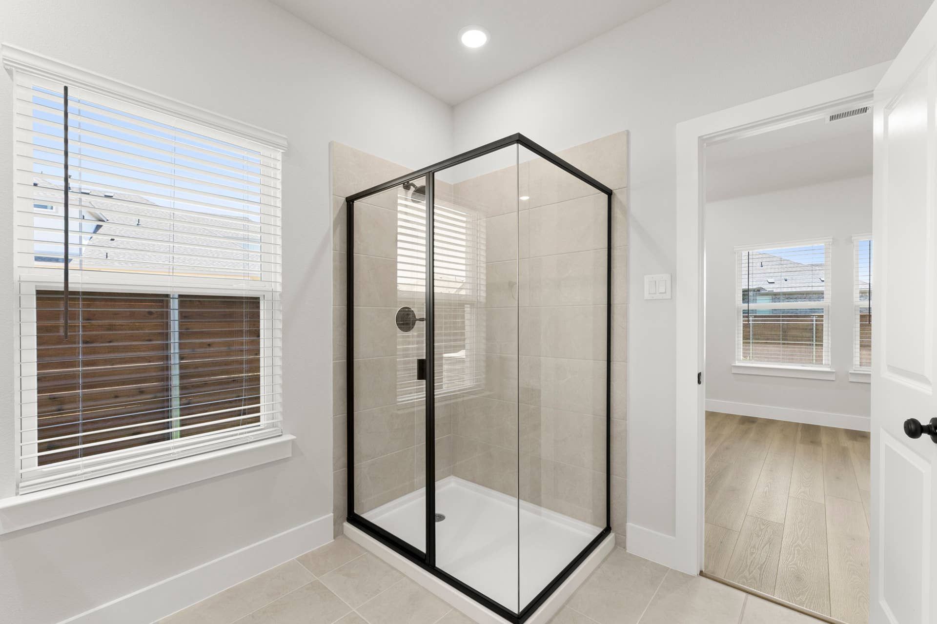 Primary bathroom with corner glass shower, tile surround, black trim, and large window