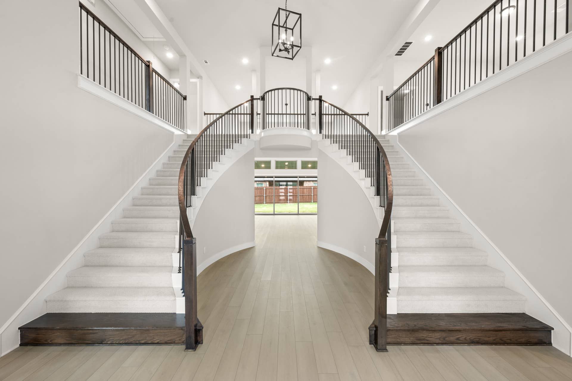 Grand entry interior with dual curved staircases, iron railings, high ceilings, and modern chandelier