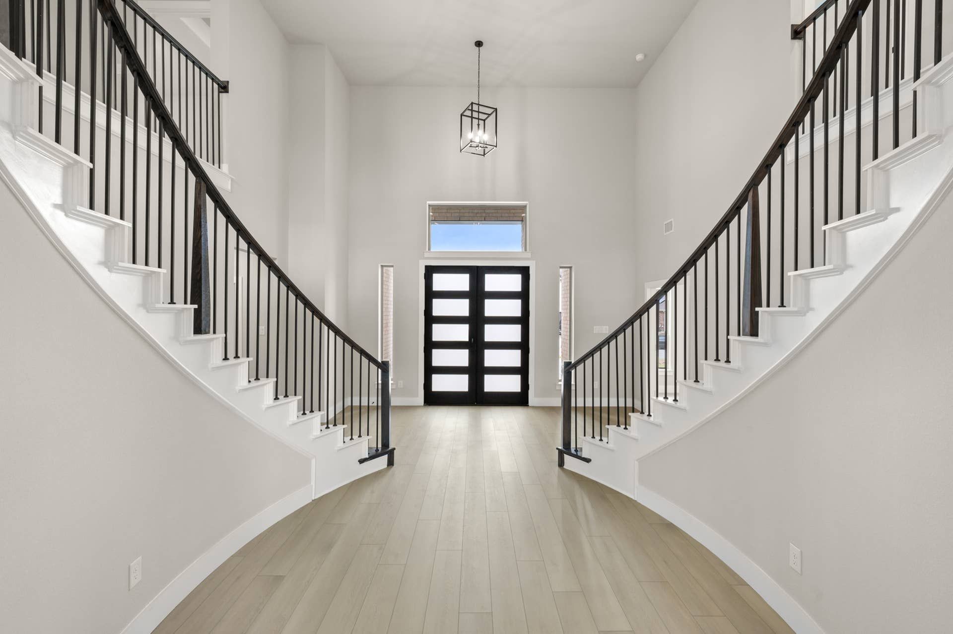 Grand two-story foyer with dual curved staircases, modern double front doors, and pendant lighting