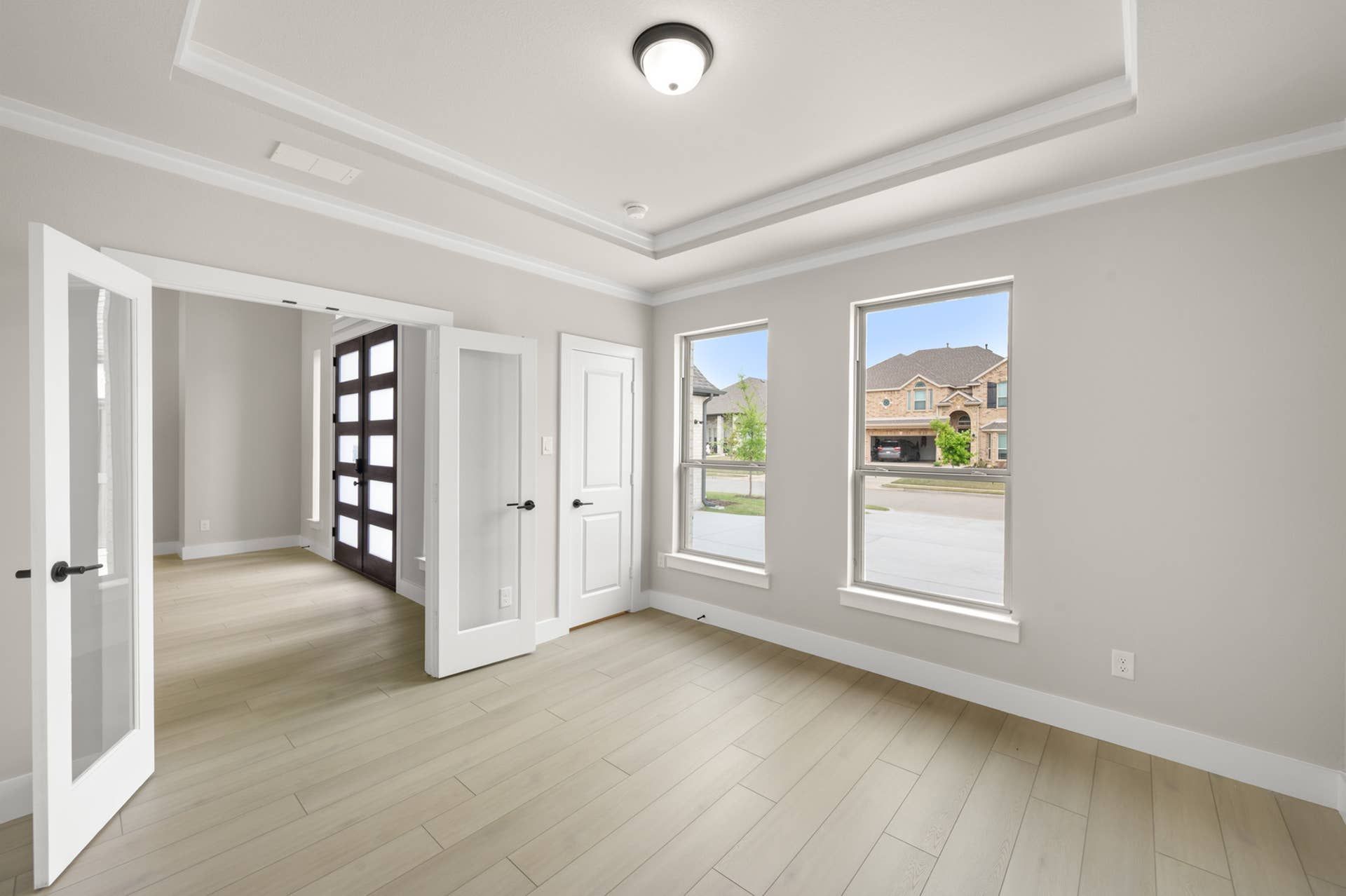 Bright study with tray ceiling, glass French doors, and front-facing windows