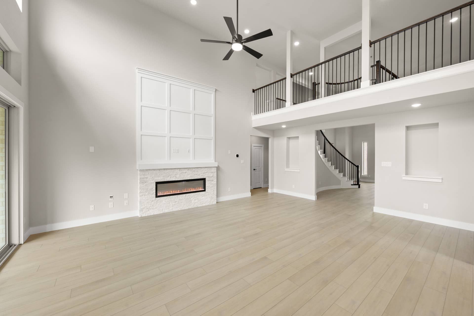 Open-concept living room with soaring ceilings, modern fireplace, loft railing, and light wood floors