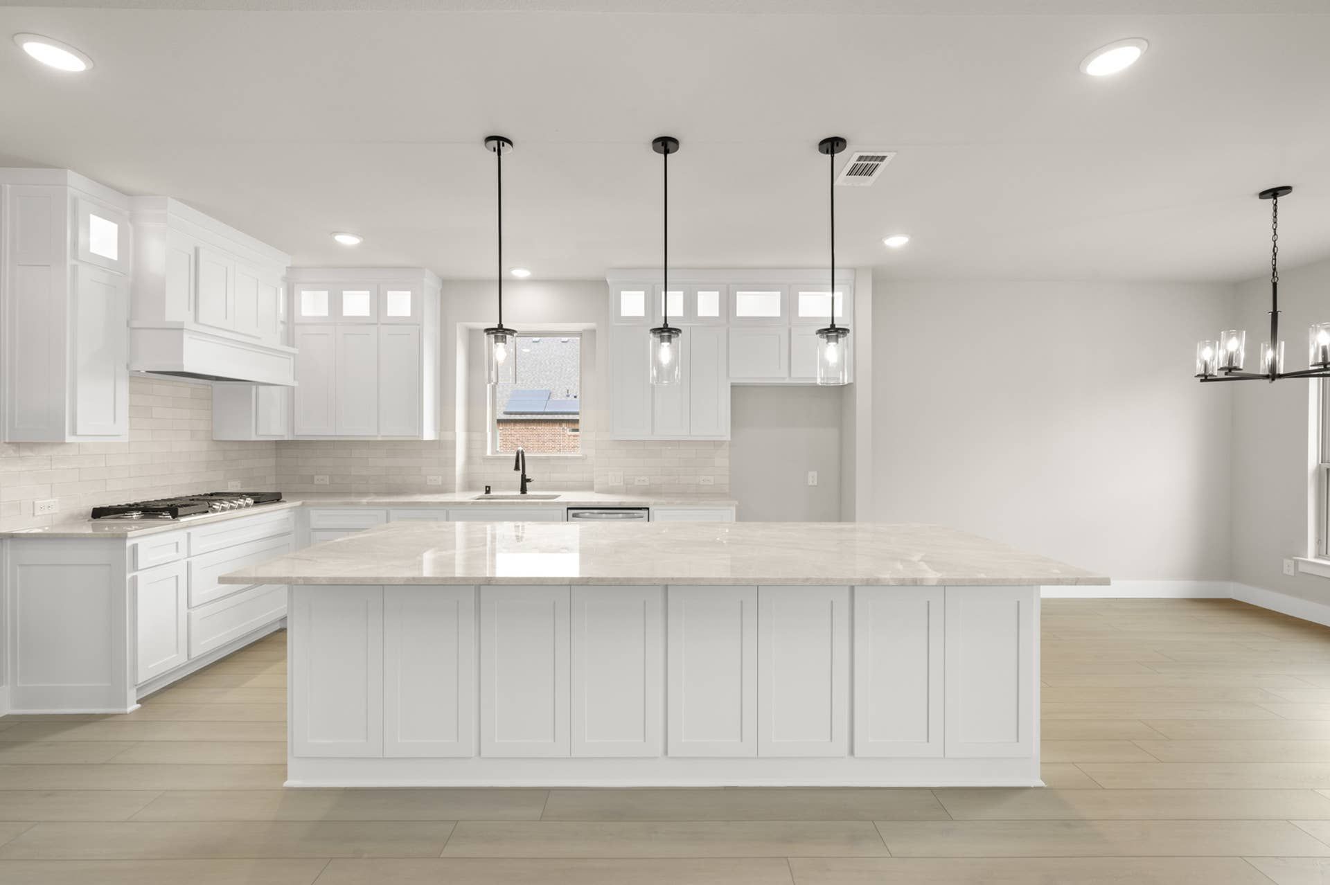 Bright white kitchen interior with oversized island, pendant lighting, and subway tile backsplash