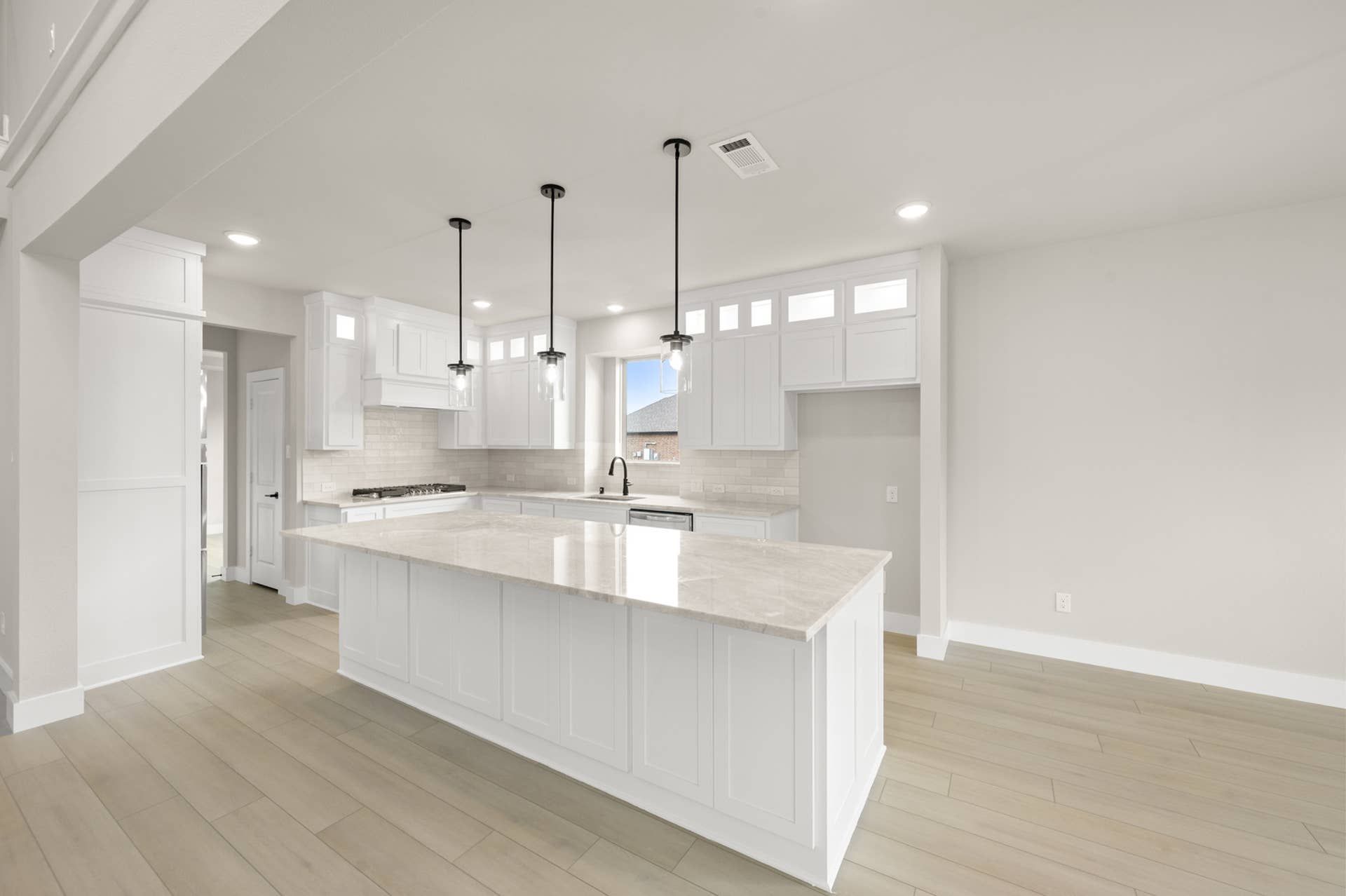 Bright kitchen interior with large island, white cabinetry, pendant lighting, and tile flooring