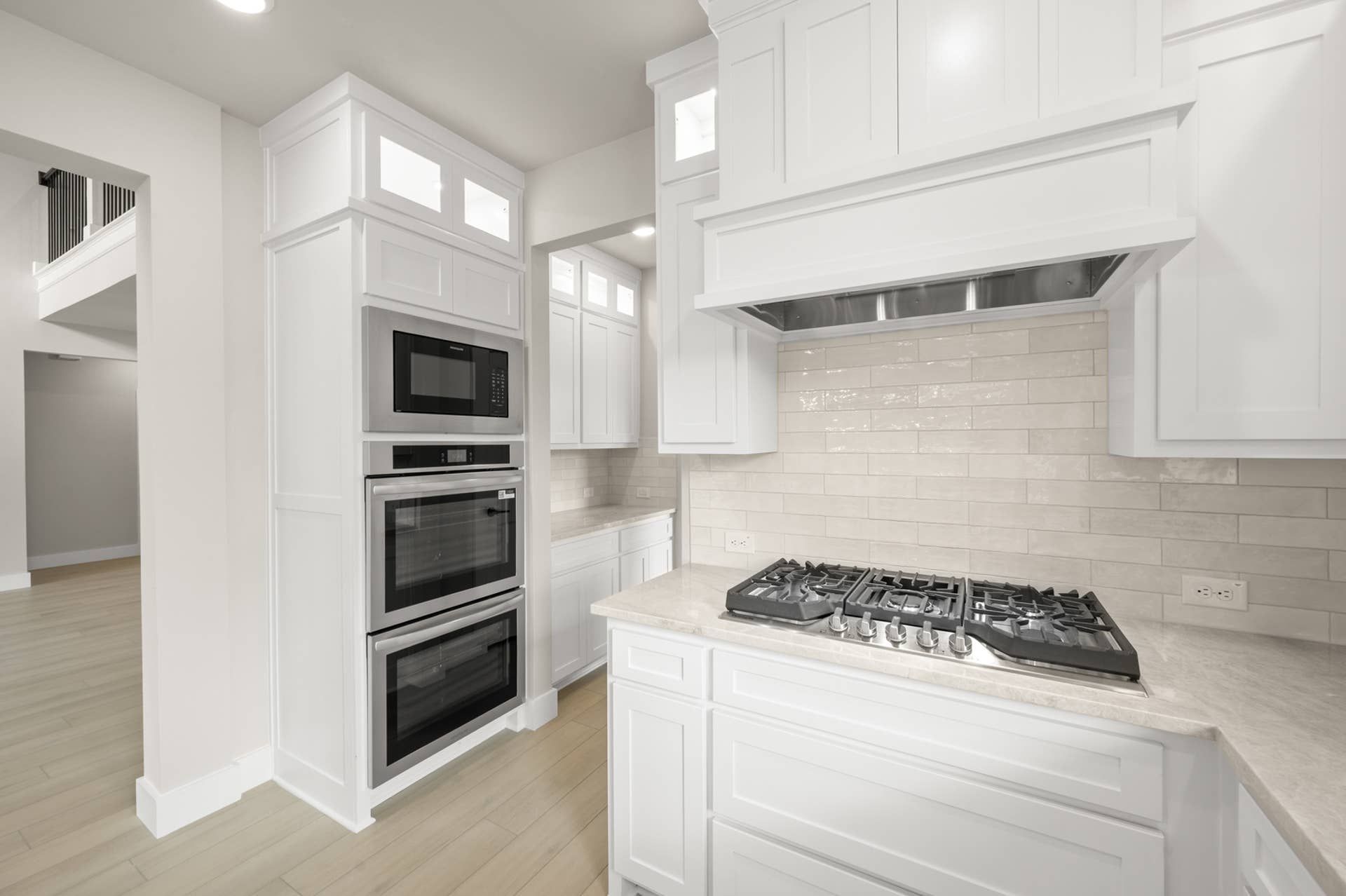 Bright kitchen with white cabinetry, gas cooktop, vent hood, and built-in double ovens