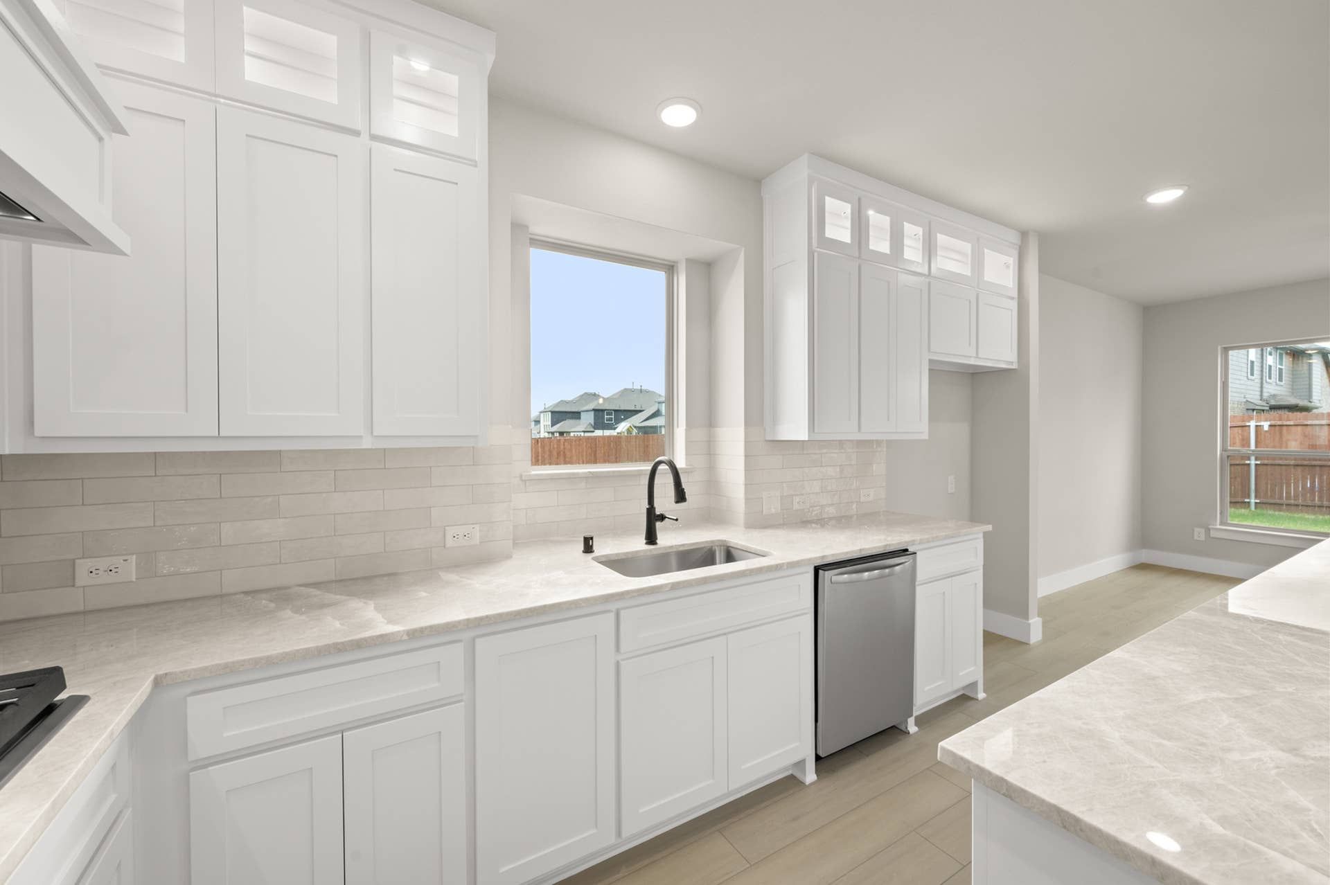 Bright kitchen interior with white shaker cabinets, quartz counters, tile backsplash, and farmhouse-style sink