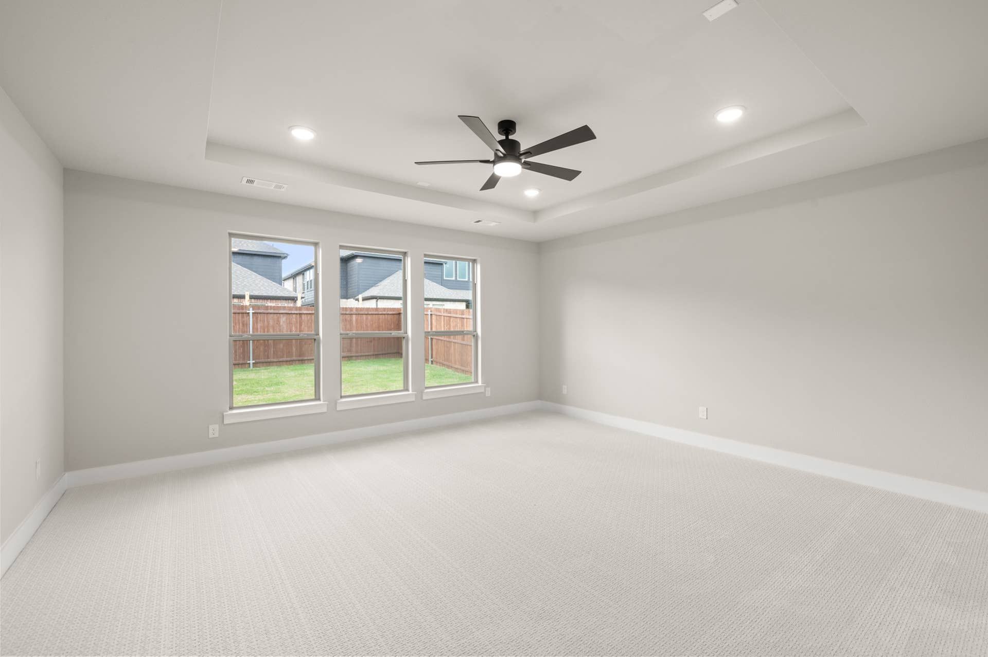 Primary suite with tray ceiling, ceiling fan, and three backyard-facing windows