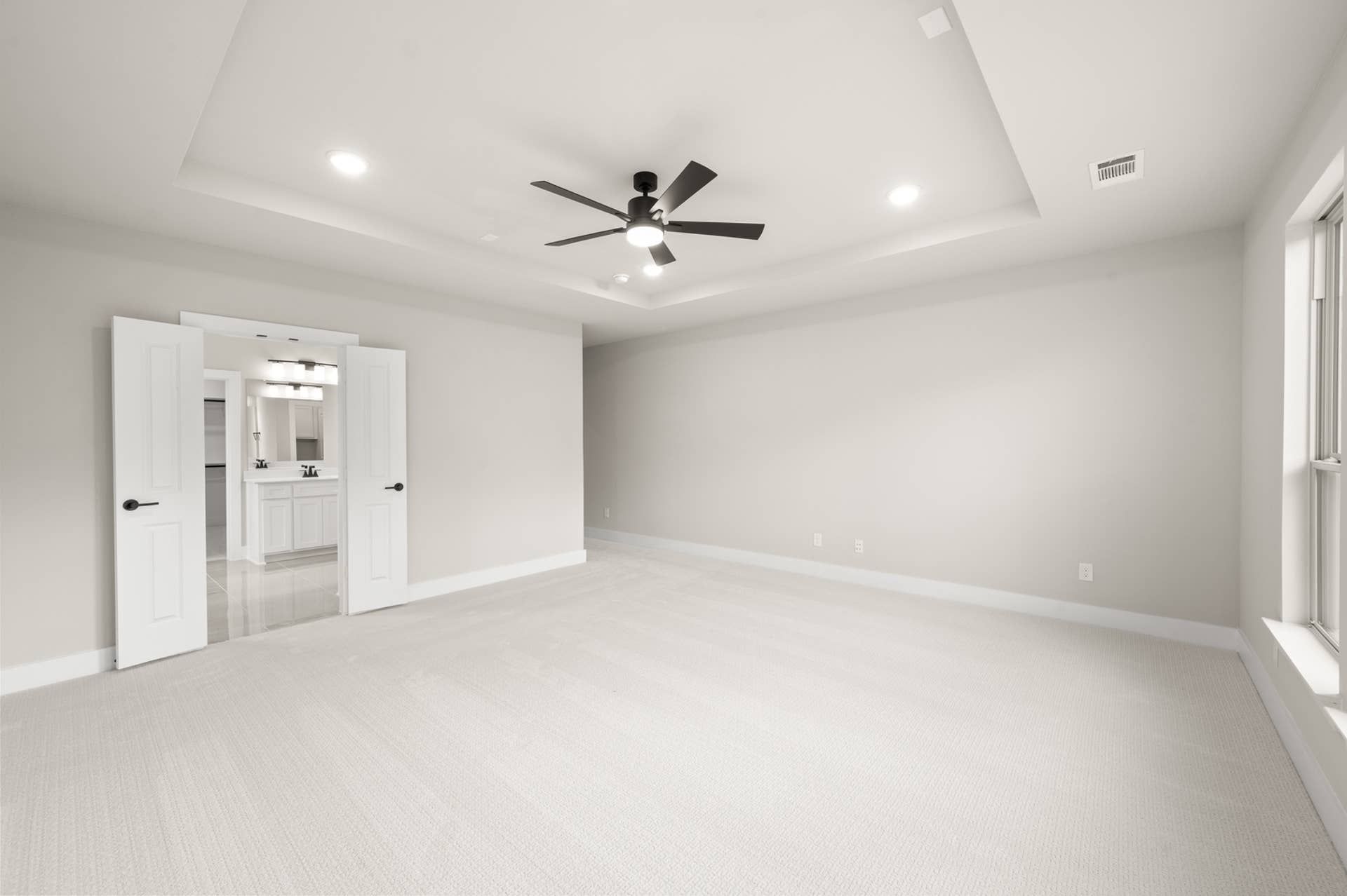 Spacious primary suite with tray ceiling, ceiling fan, and ensuite bath access