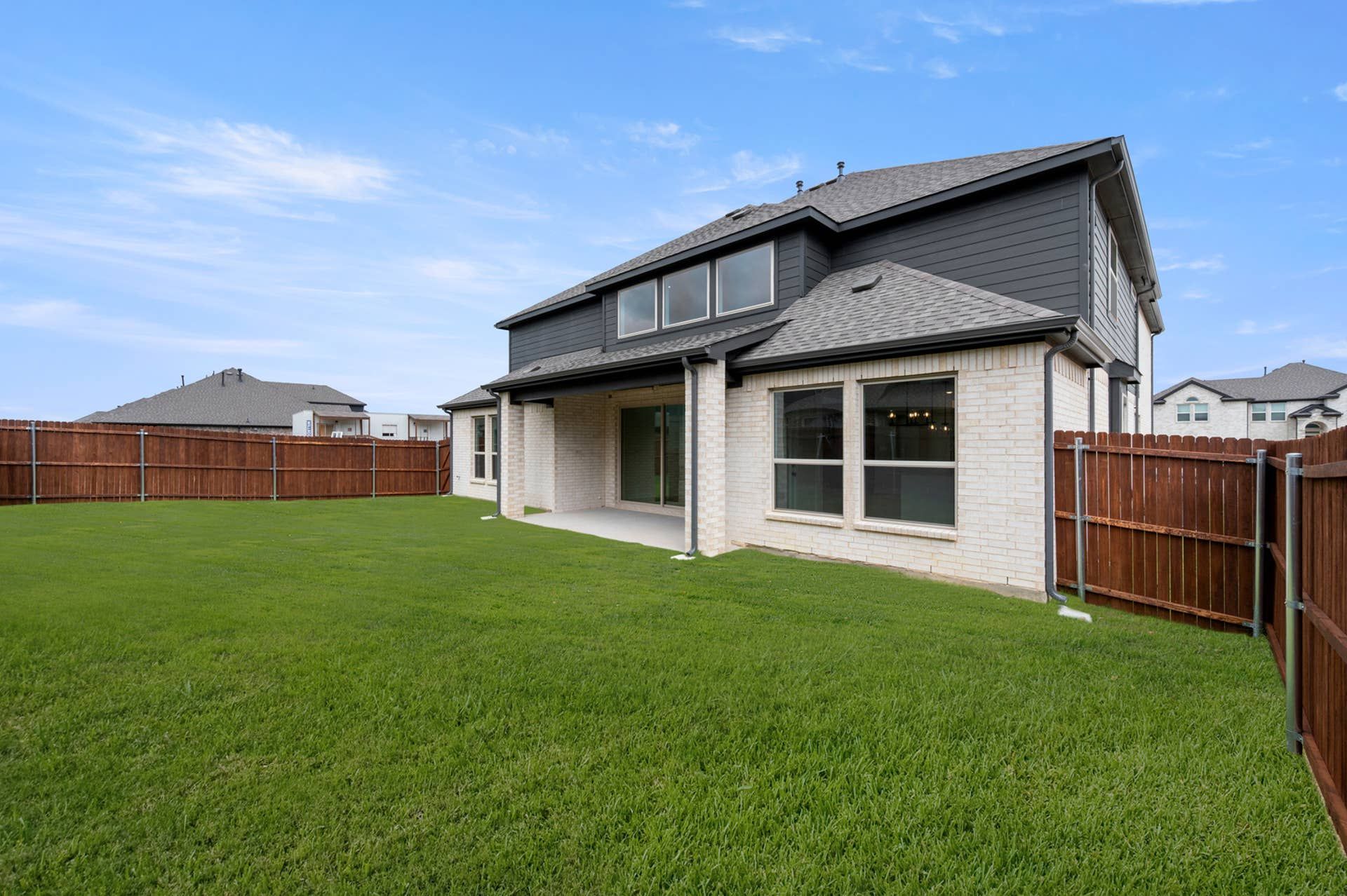 Rear exterior elevation with covered patio, fenced backyard, and two-story brick home