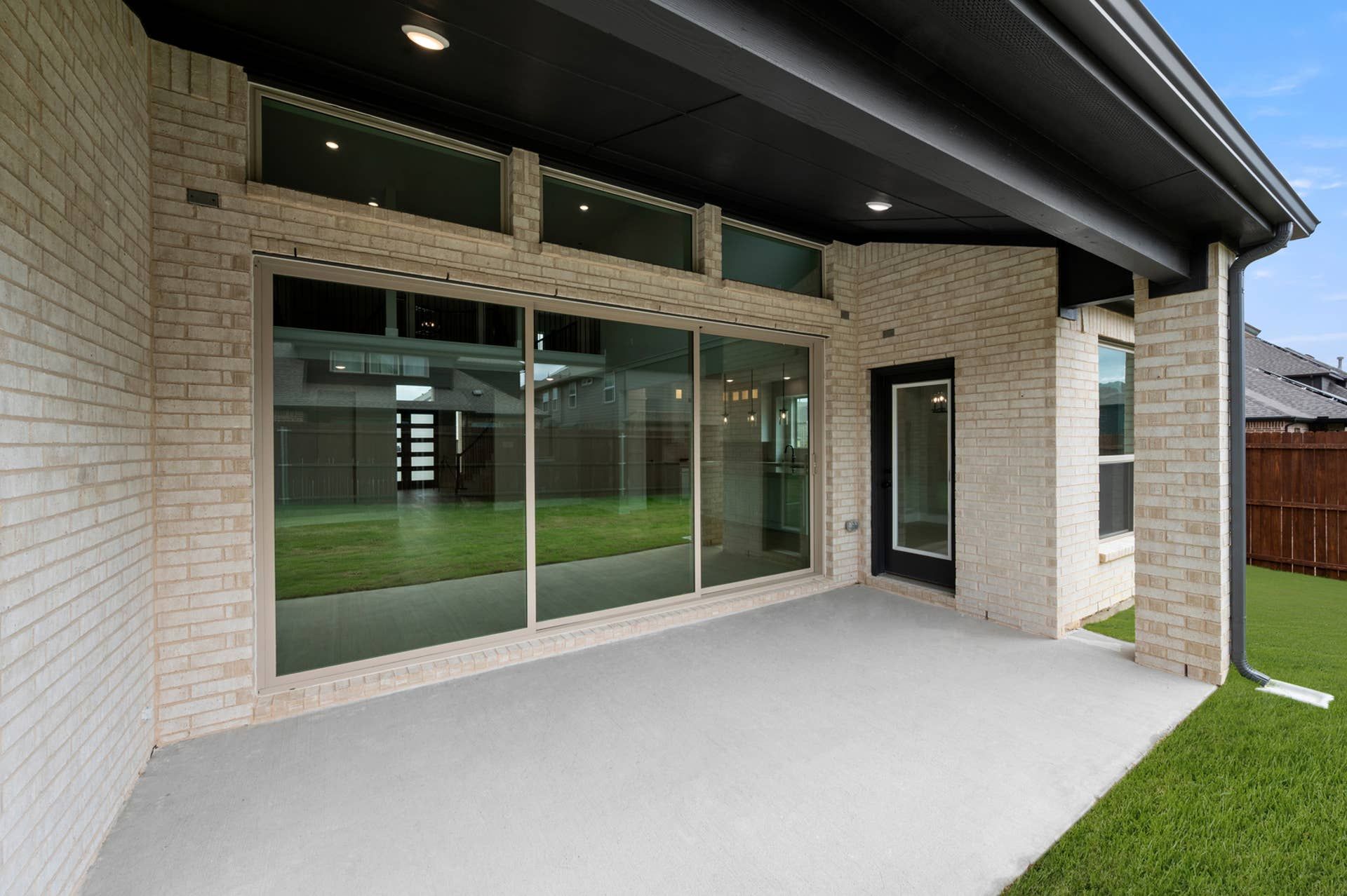 Covered rear patio with brick exterior, large sliding glass doors, and backyard access