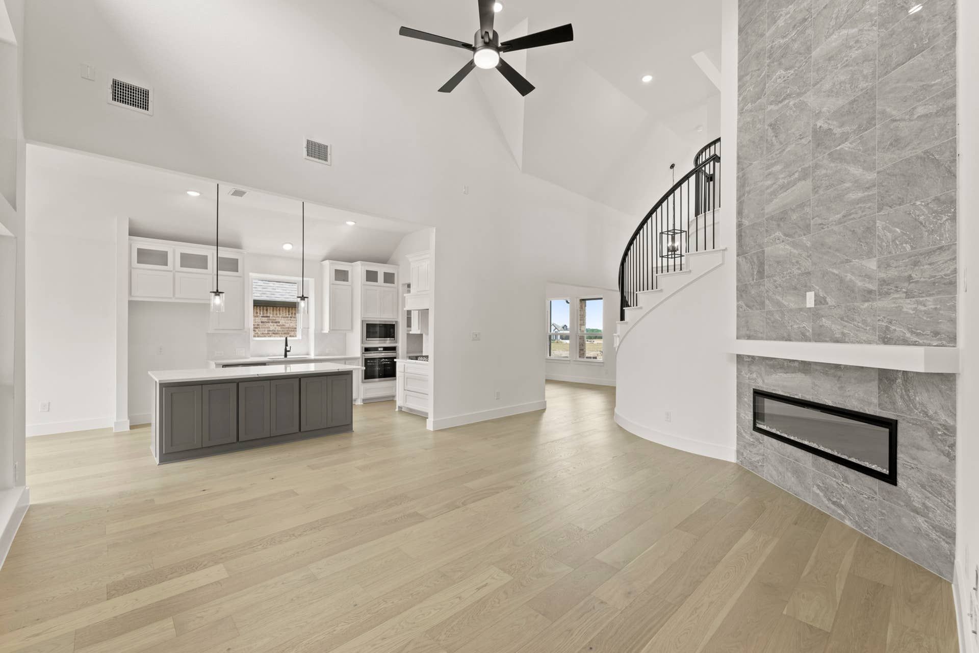 Spacious open-concept living area with modern kitchen, curved staircase, and elegant fireplace.